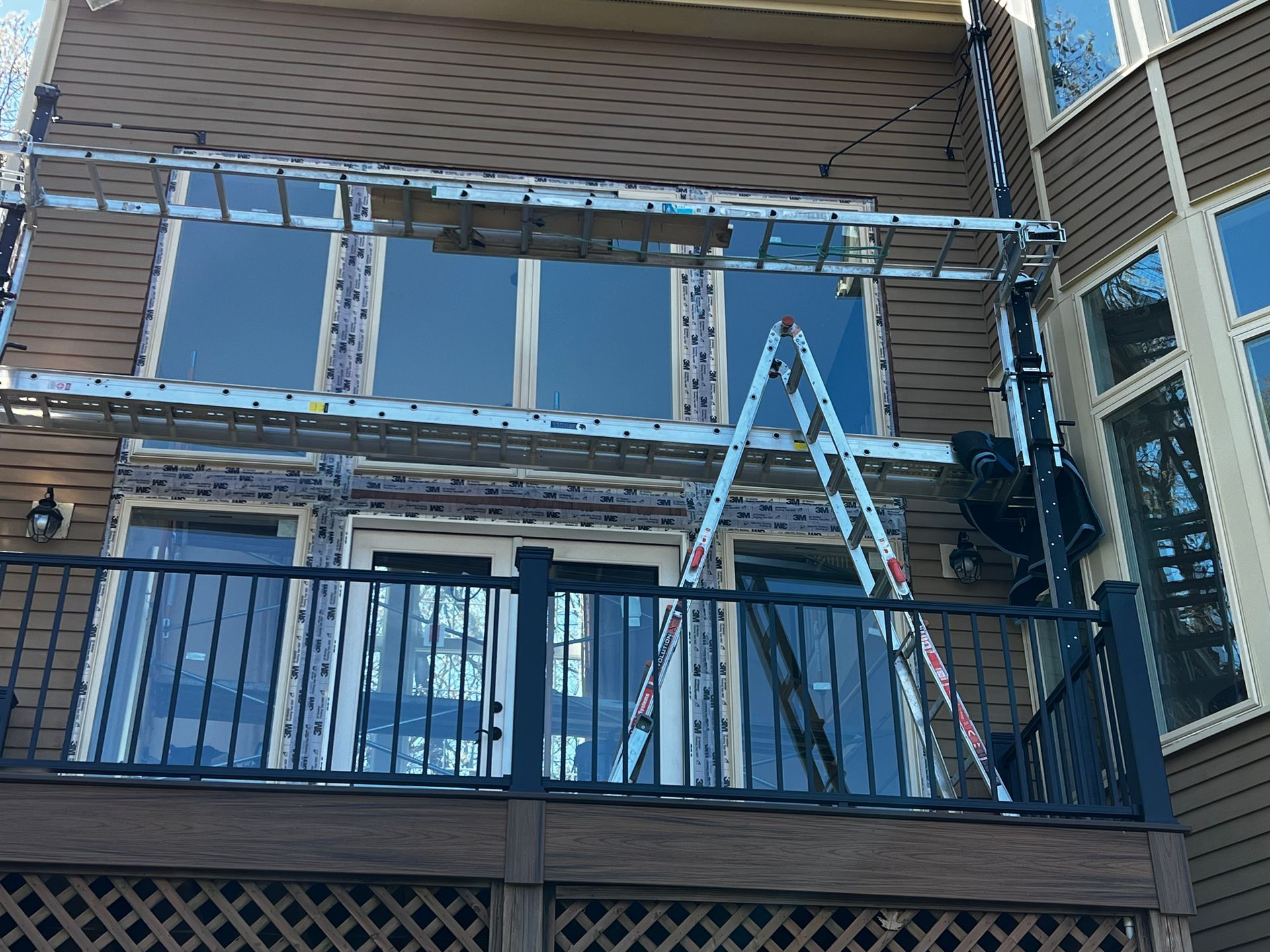 Person on a ladder working on a house balcony with exposed framing and blue sheathing
