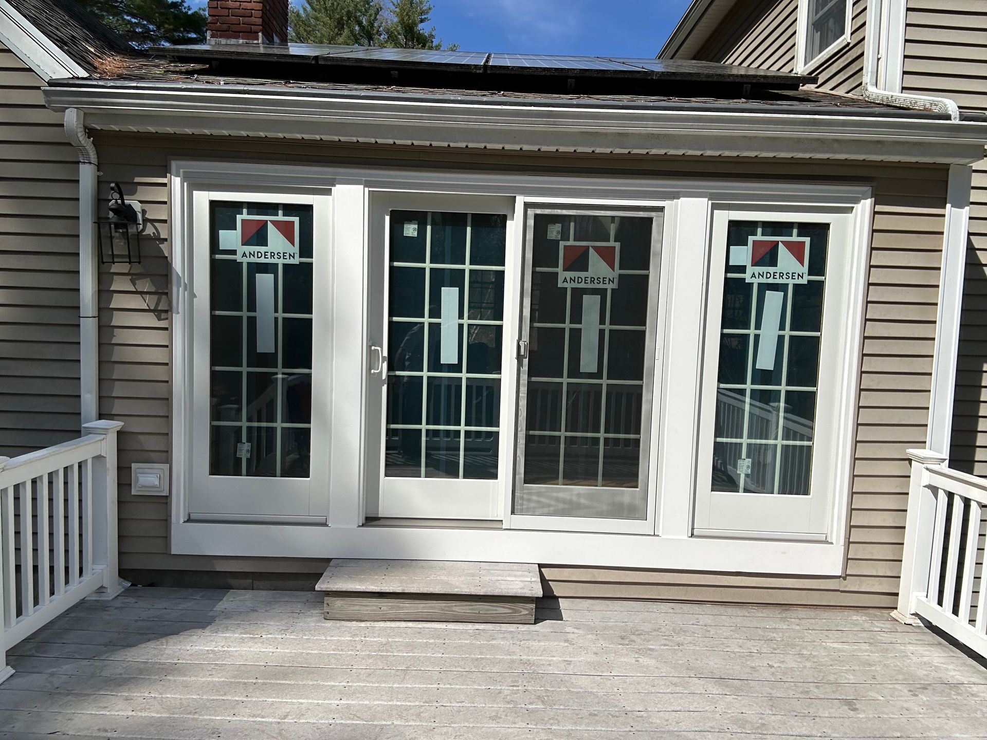 White French doors with glass panes and side windows on a gray house exterior, opening onto a deck.