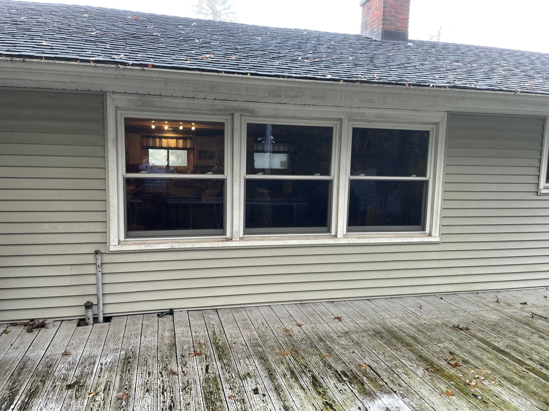 Side of a house with three windows and a weathered wooden deck.