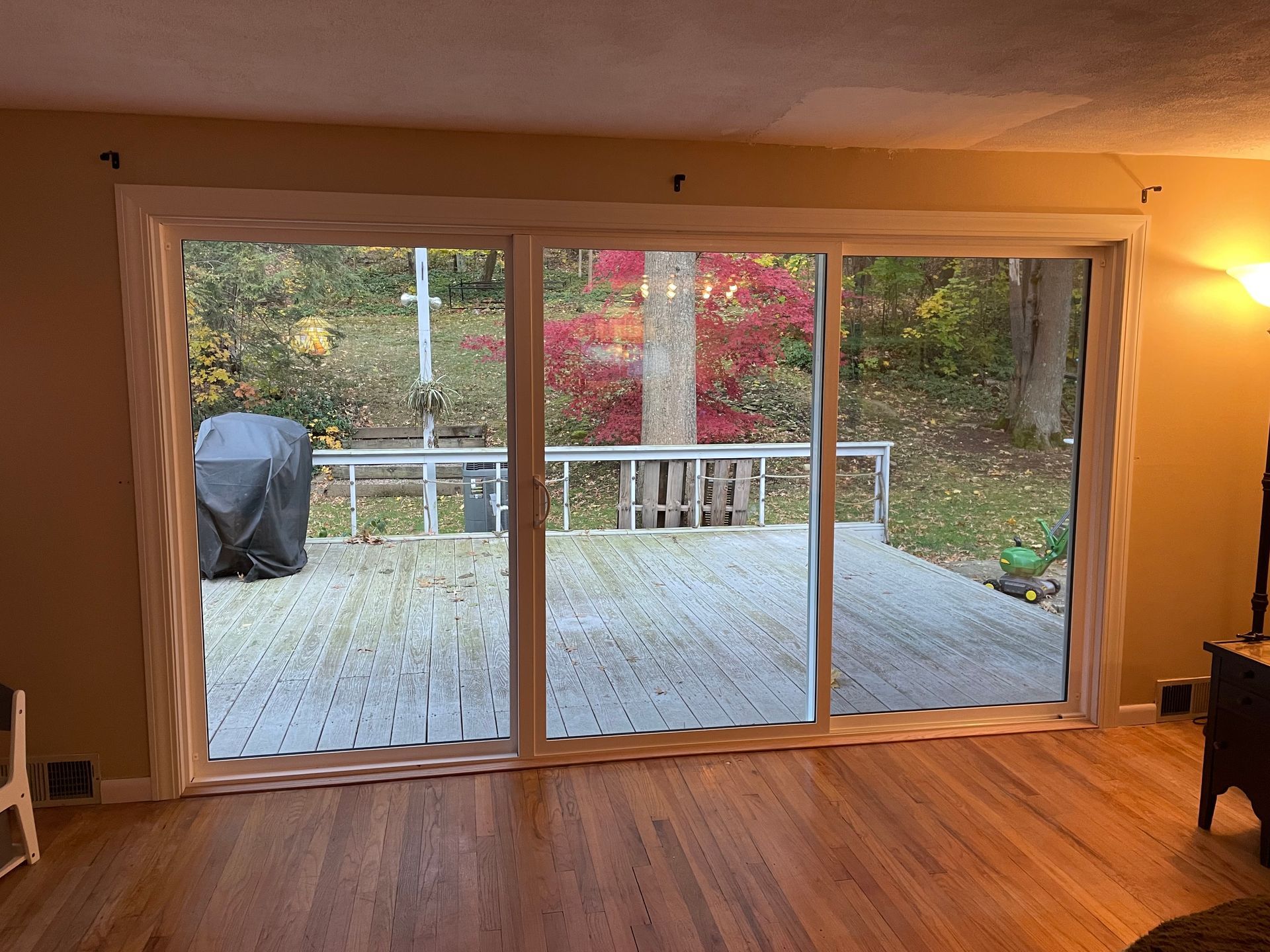 Living room with large sliding glass doors opening to a deck and autumn trees outside