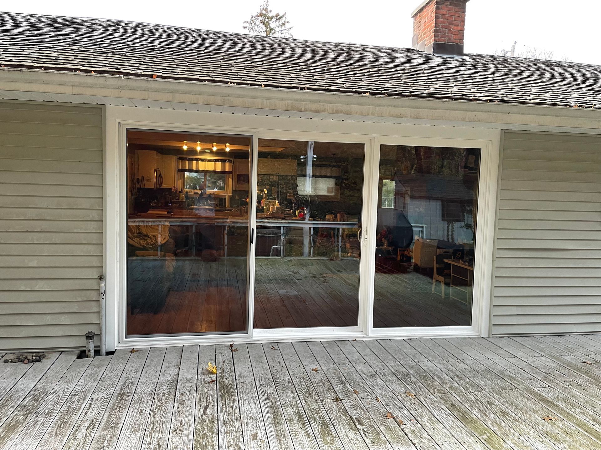 Backyard deck with sliding glass doors, beige siding, and a roof overhang lit warmly inside