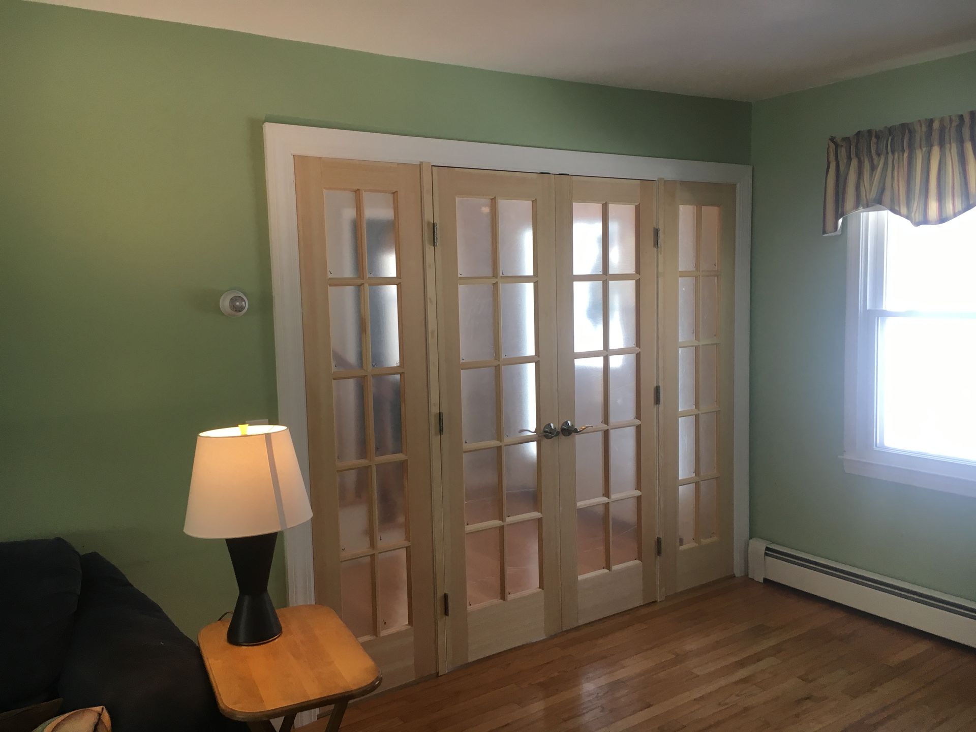 Living room with green walls, French doors, a lit lamp, and a bright window.
