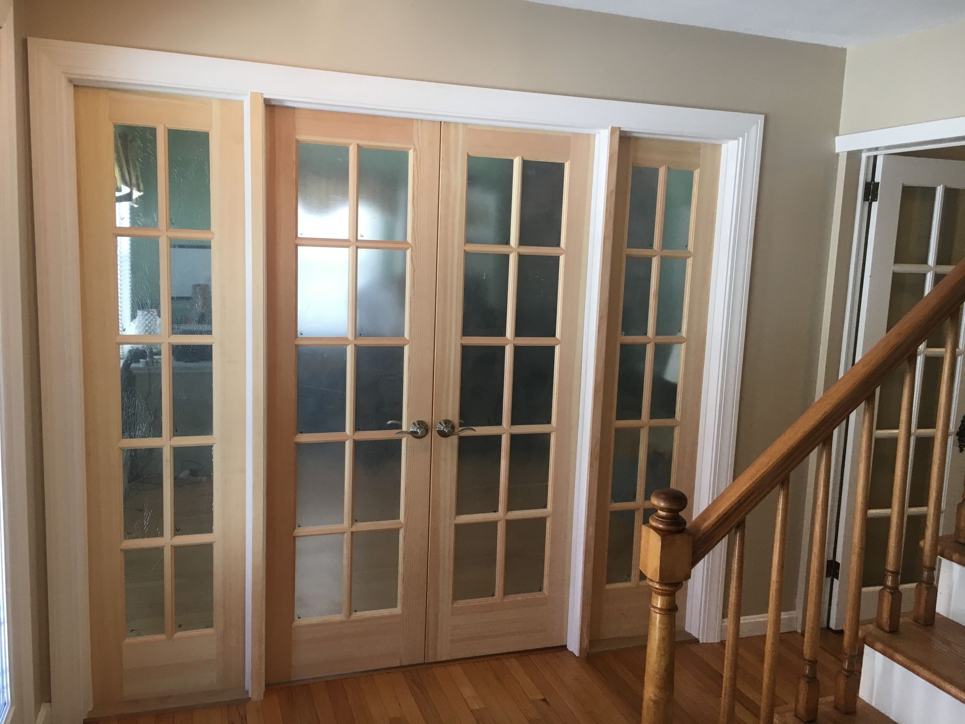 White French doors with glass panes in a hallway beside a wooden staircase.