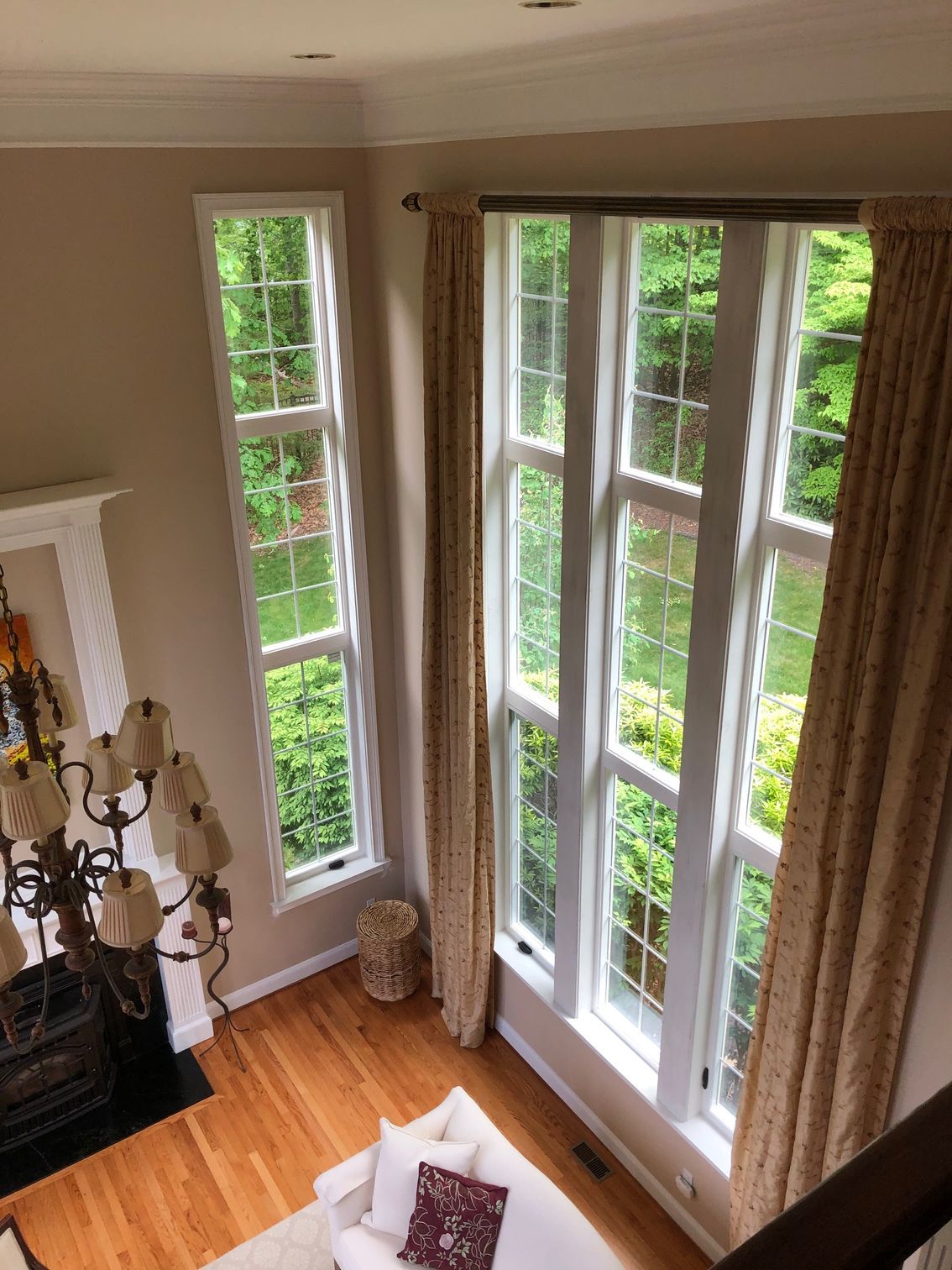 Bright living room corner with tall windows, beige curtains, hardwood floor, and a fireplace