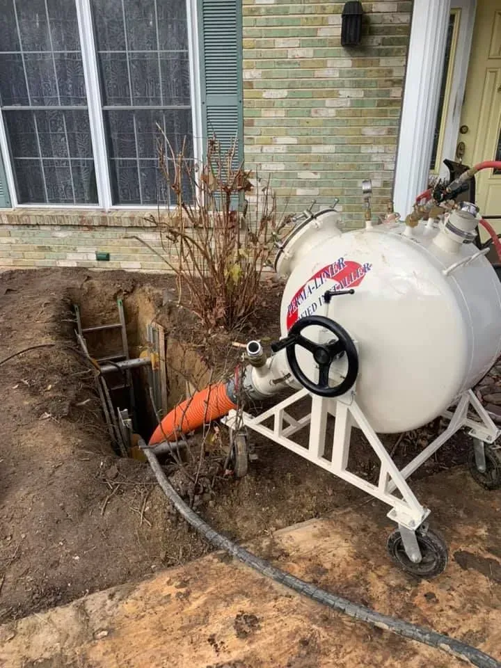 A large white tank connected to a trench by an orange hose, outside a brick building.