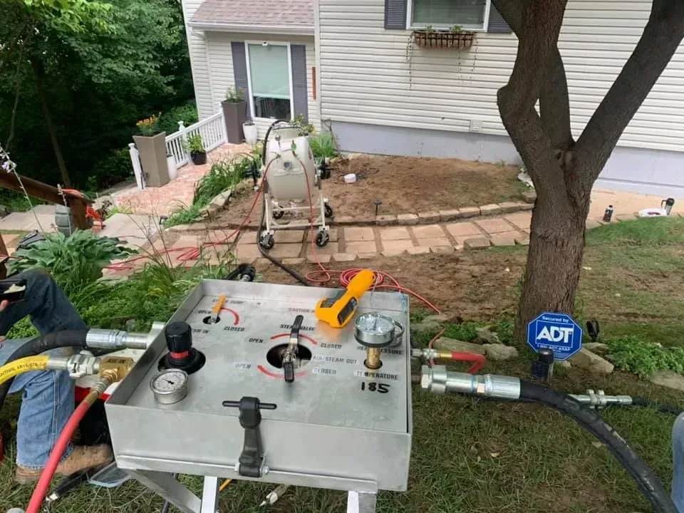 Silver control box with gauges and hoses in front of a house, possibly related to landscaping.