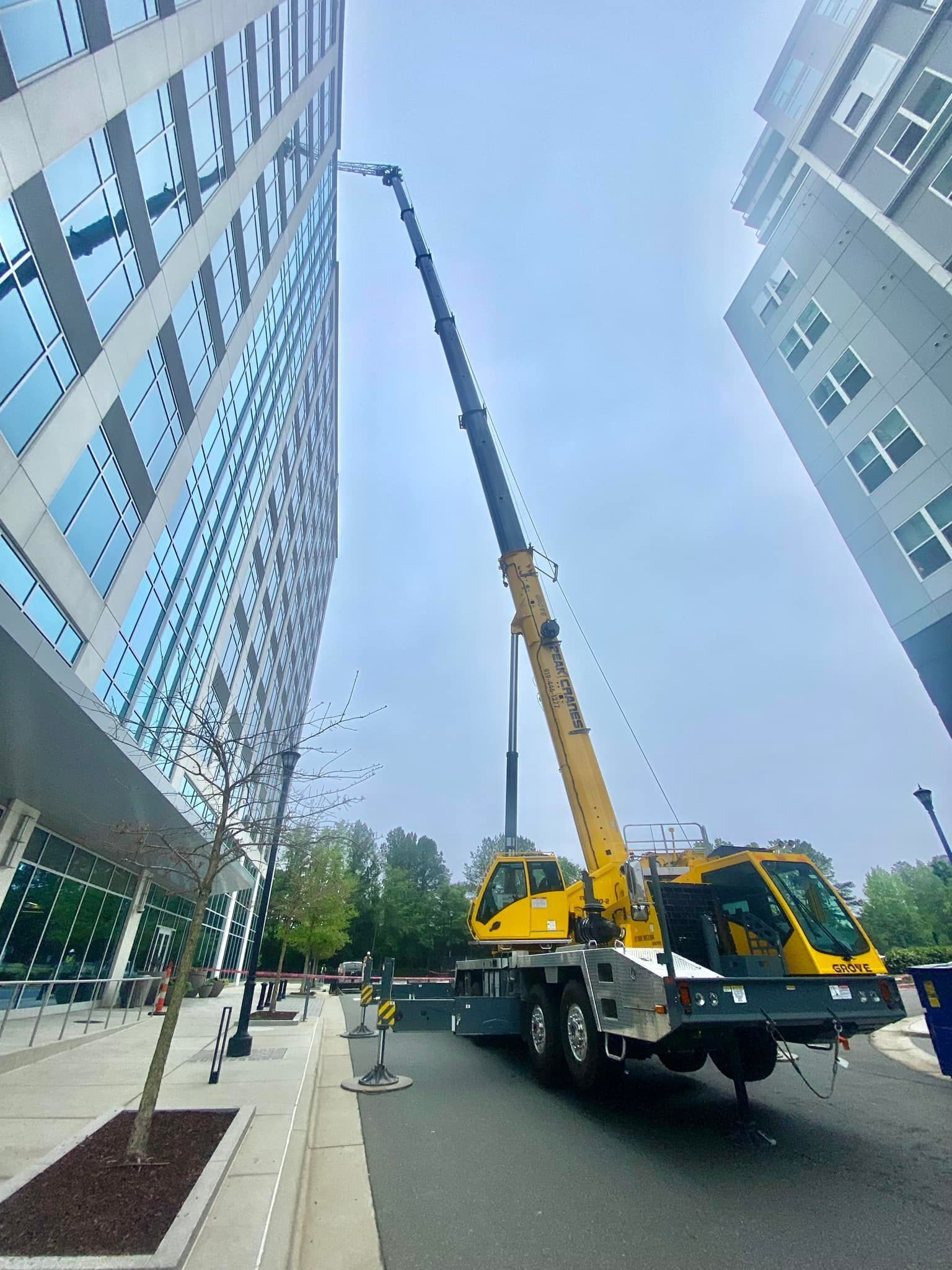 Yellow crane extending toward a tall glass building on a street; blue sky above.