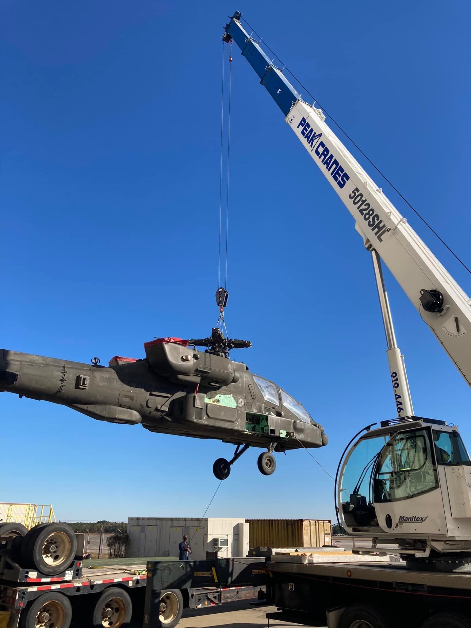 A helicopter being lifted by a crane onto a flatbed trailer under a blue sky.