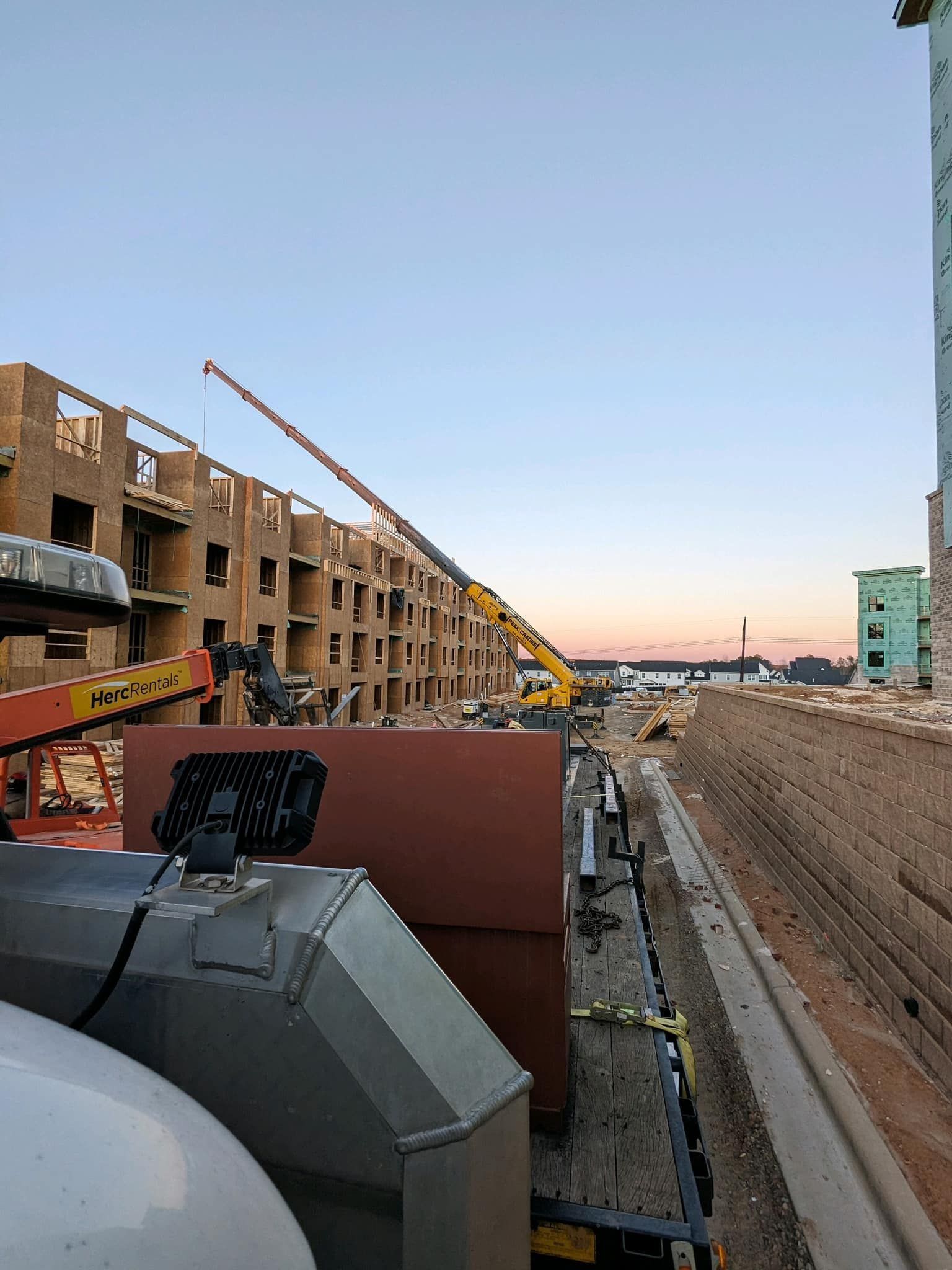Construction site with crane lifting materials to a multi-story building frame at dusk.