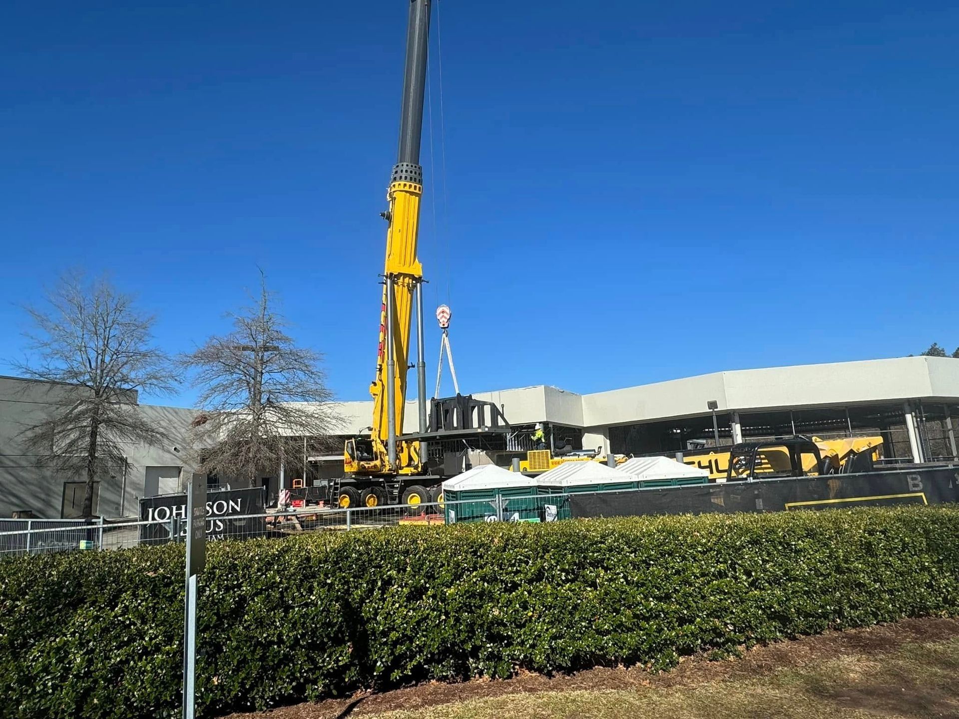 Construction site with crane, workers, and building under blue sky.