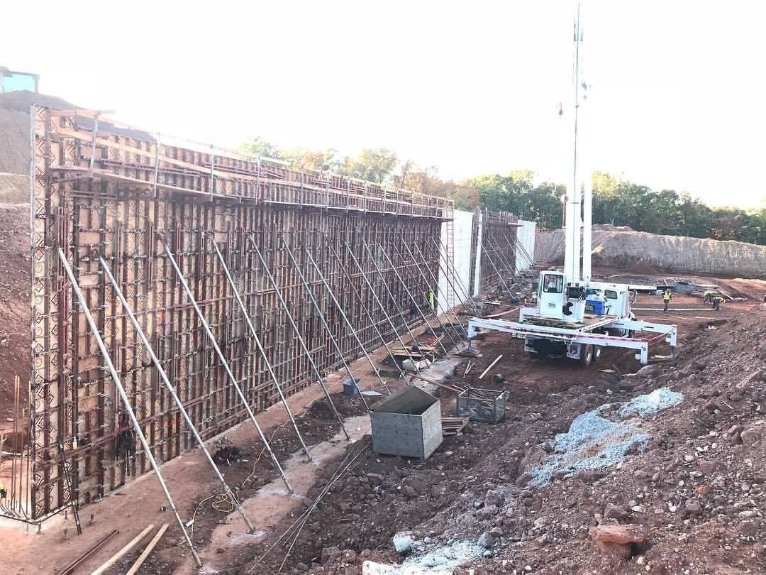 Construction site with wooden formwork for a retaining wall, a crane, and a partially built structure.