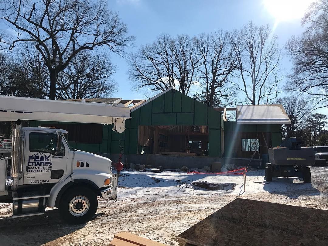Construction site with snow, a truck, and a partially built green house under a sunny sky.