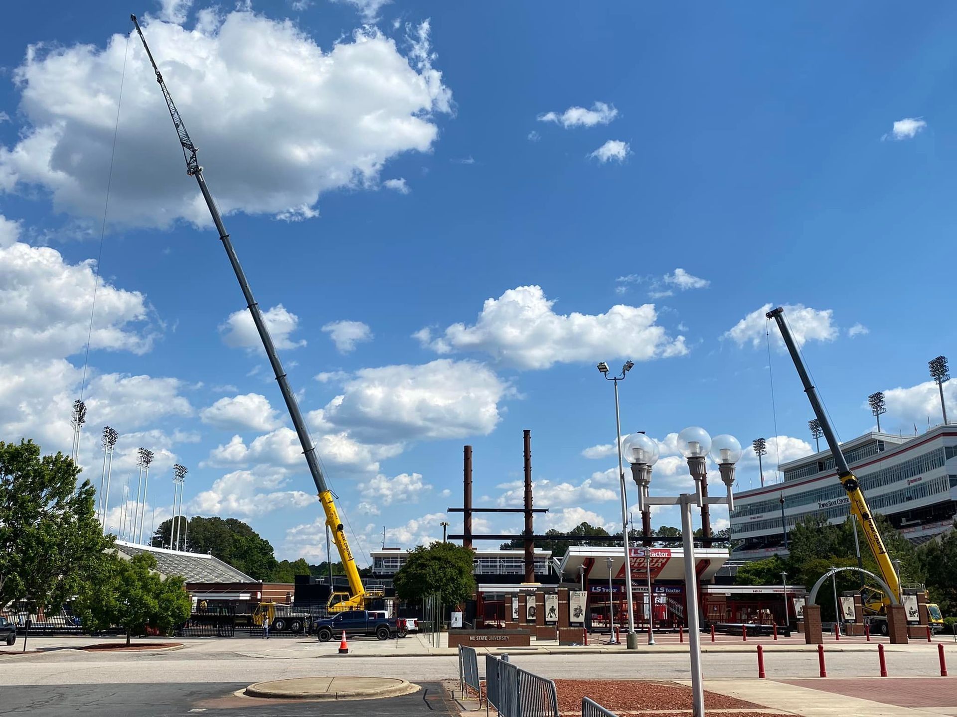 Two yellow cranes in a bright blue sky with clouds, possibly at a construction site.