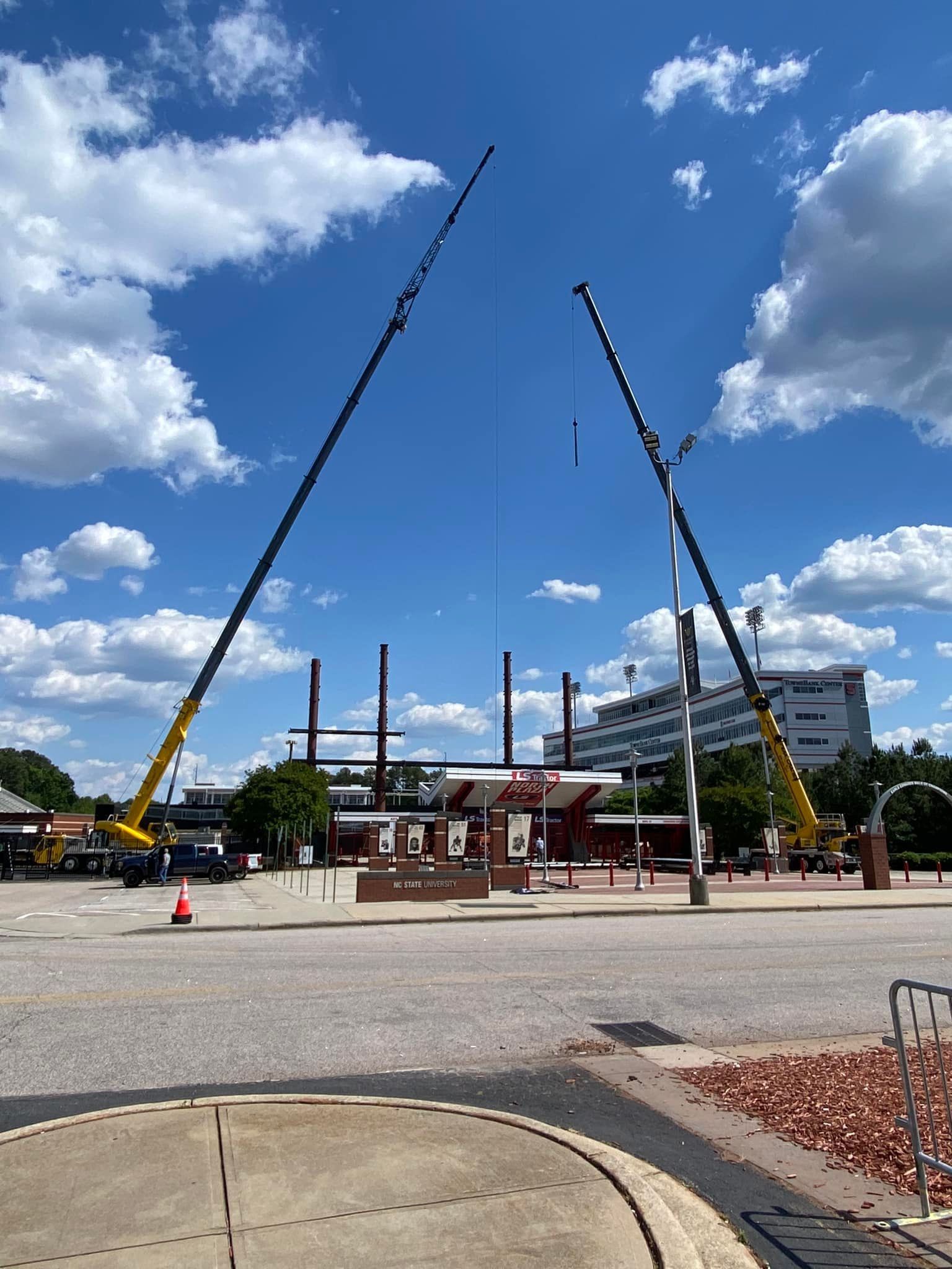 Two tall yellow cranes supporting a sling shot ride in an open lot on a sunny day.