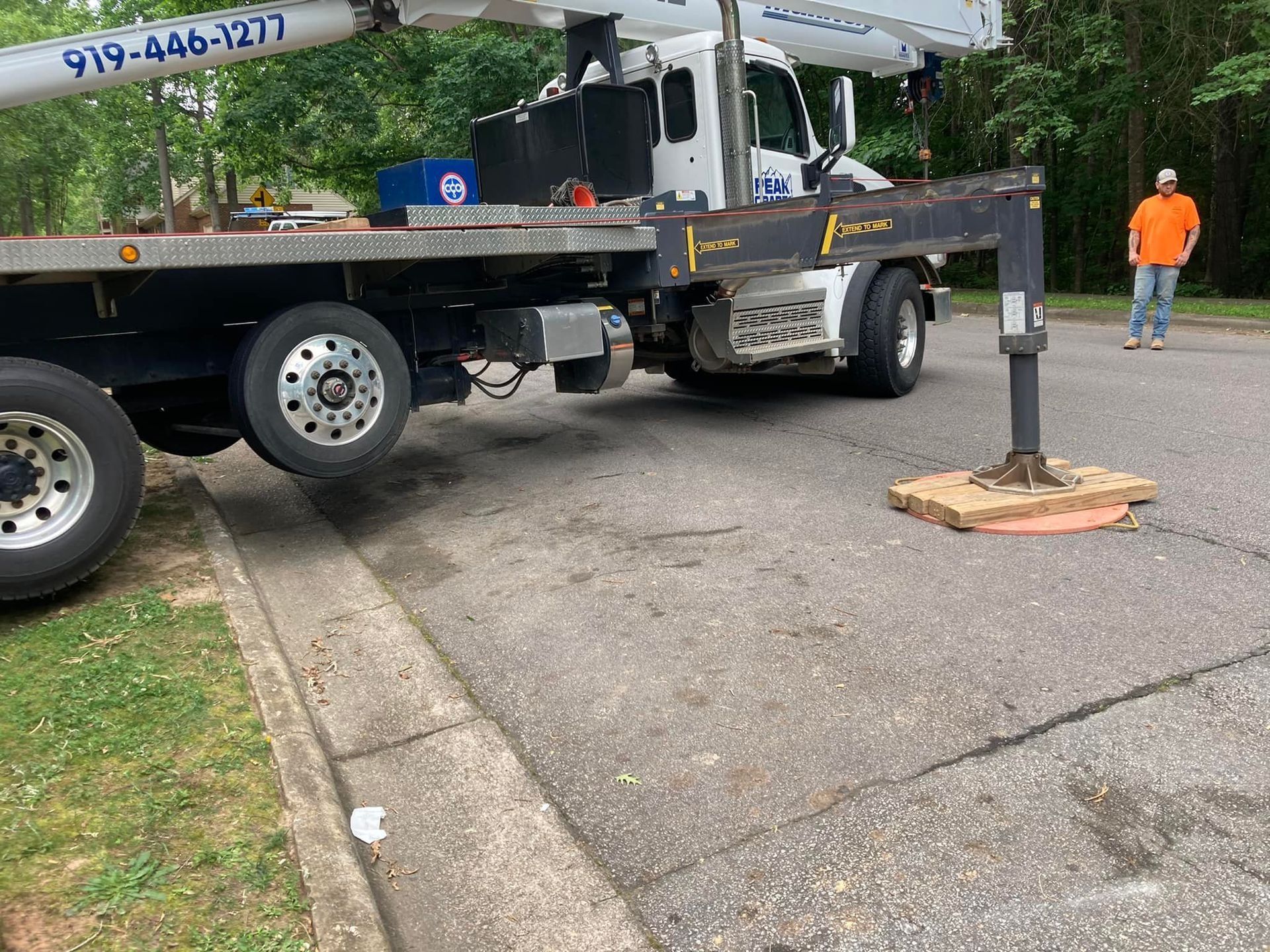 Truck with crane on road, supporting beam, person in orange shirt nearby.