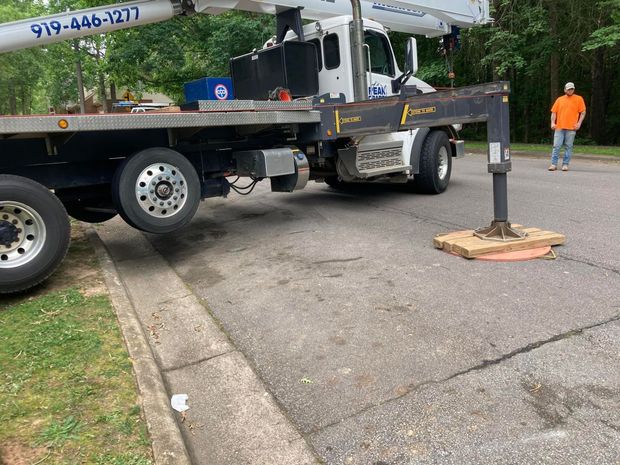 Truck with crane on road, supporting beam, person in orange shirt nearby.