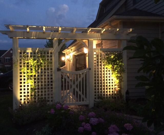 A pergola is lit up at night in front of a house
