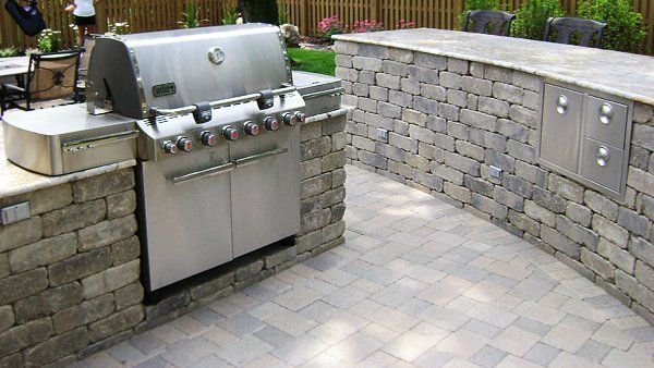 A stainless steel grill is sitting on a brick patio next to a stone wall.