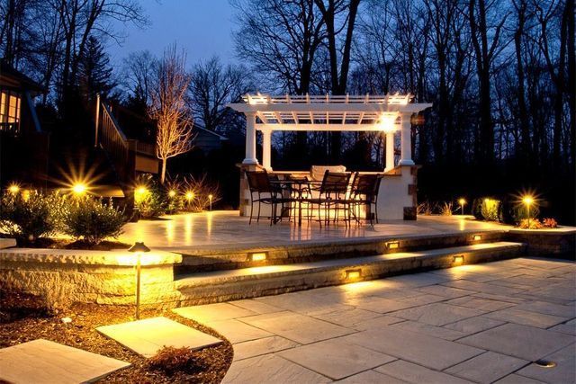 A patio with a pergola and tables and chairs at night