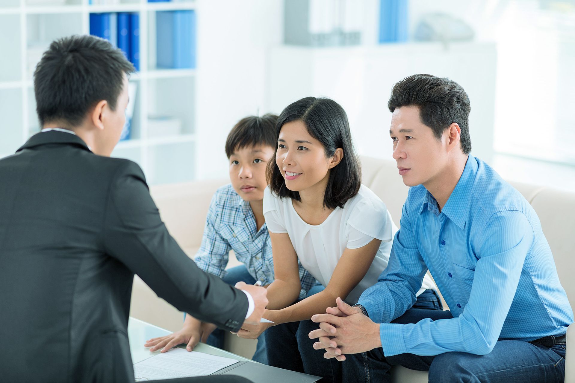 Therapist with clipboard observes a boy playing with a spinning top; parents sit on sofa, looking on.
