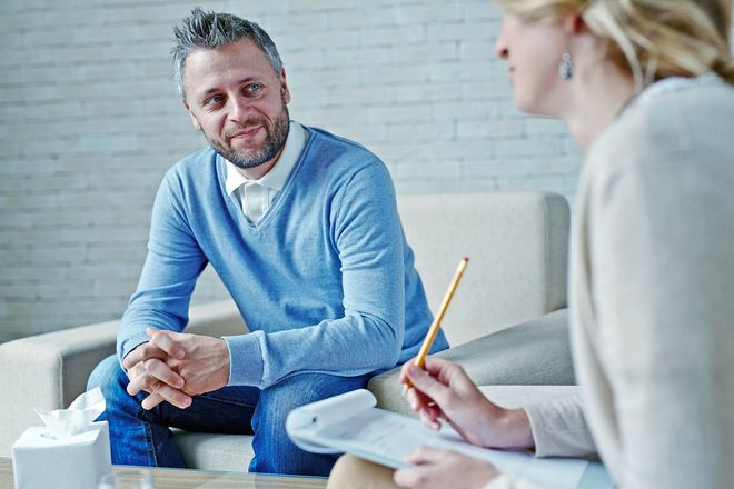 Woman on couch talking to therapist in a light-filled room.