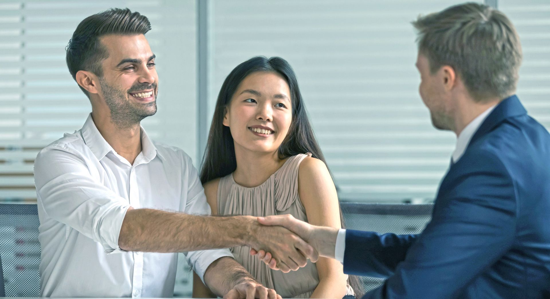 Couple on blue couch smiles at therapist, who is taking notes. Neutral-colored room.