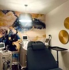 Treatment room with a dark reclined chair, medical equipment, and an abstract mural. Two golden wall decorations are on the right.