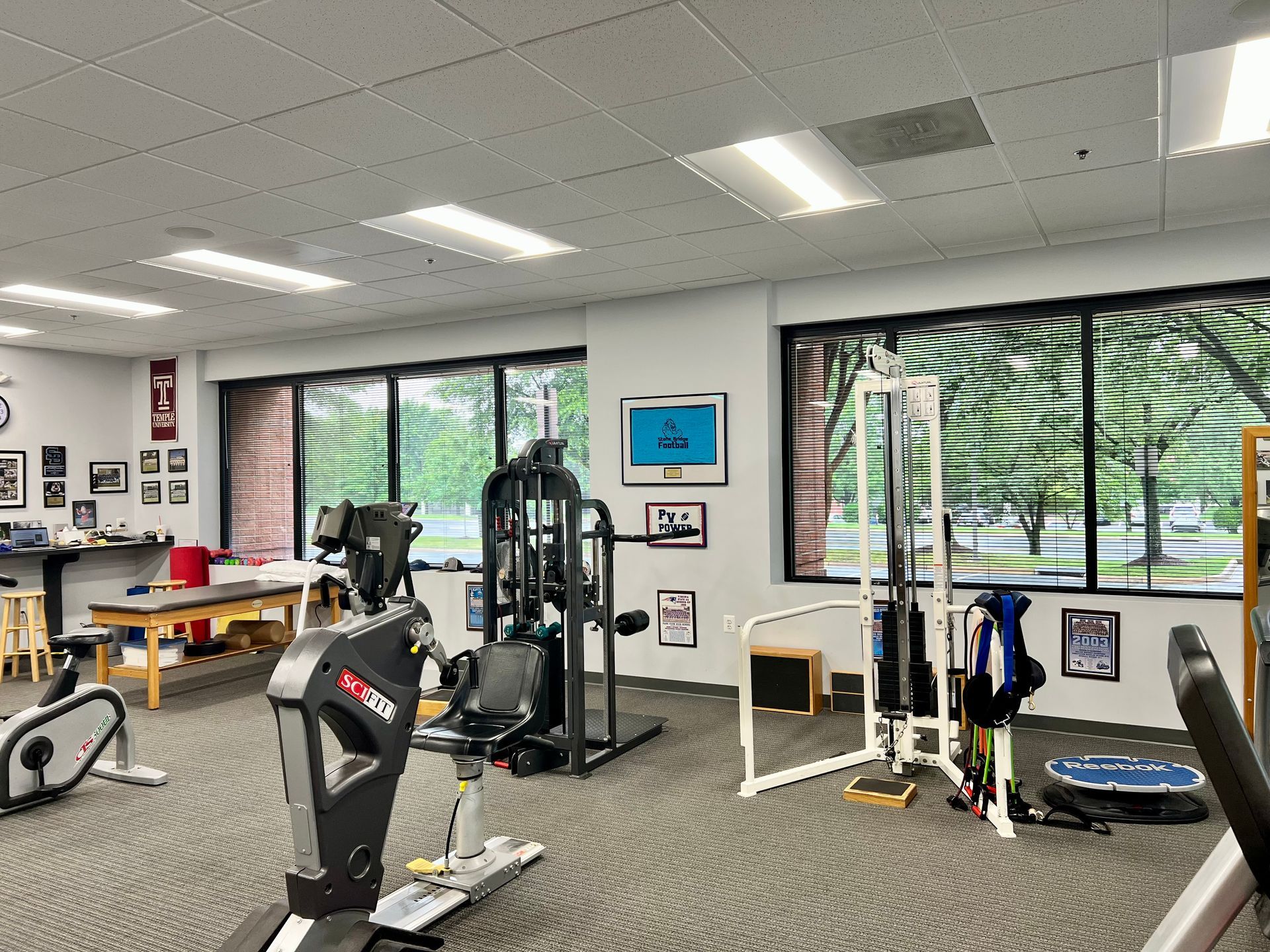 A gym with a lot of exercise equipment and a lot of windows.