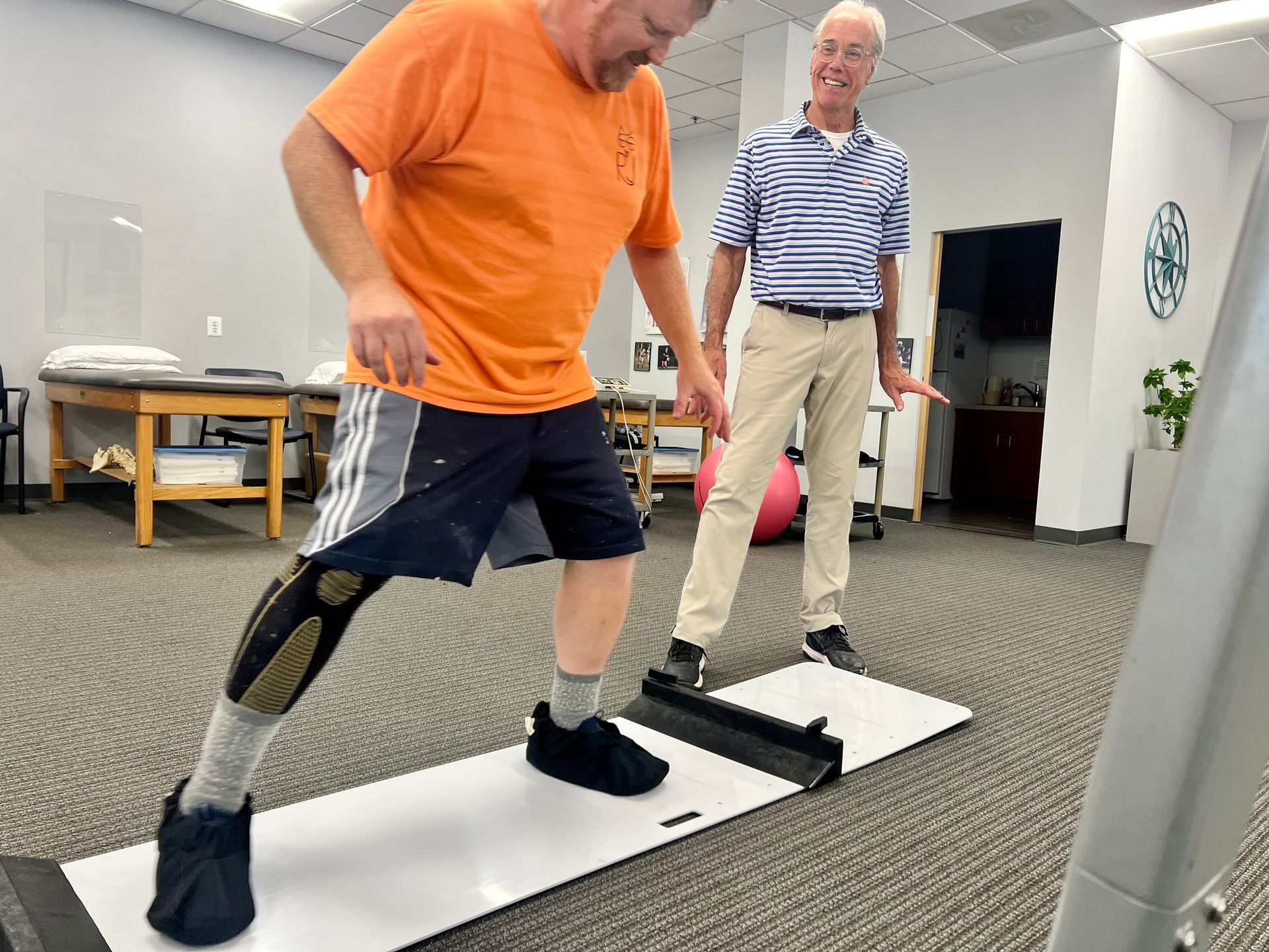 Man with prosthetic leg practices walking with a therapist in a clinic.