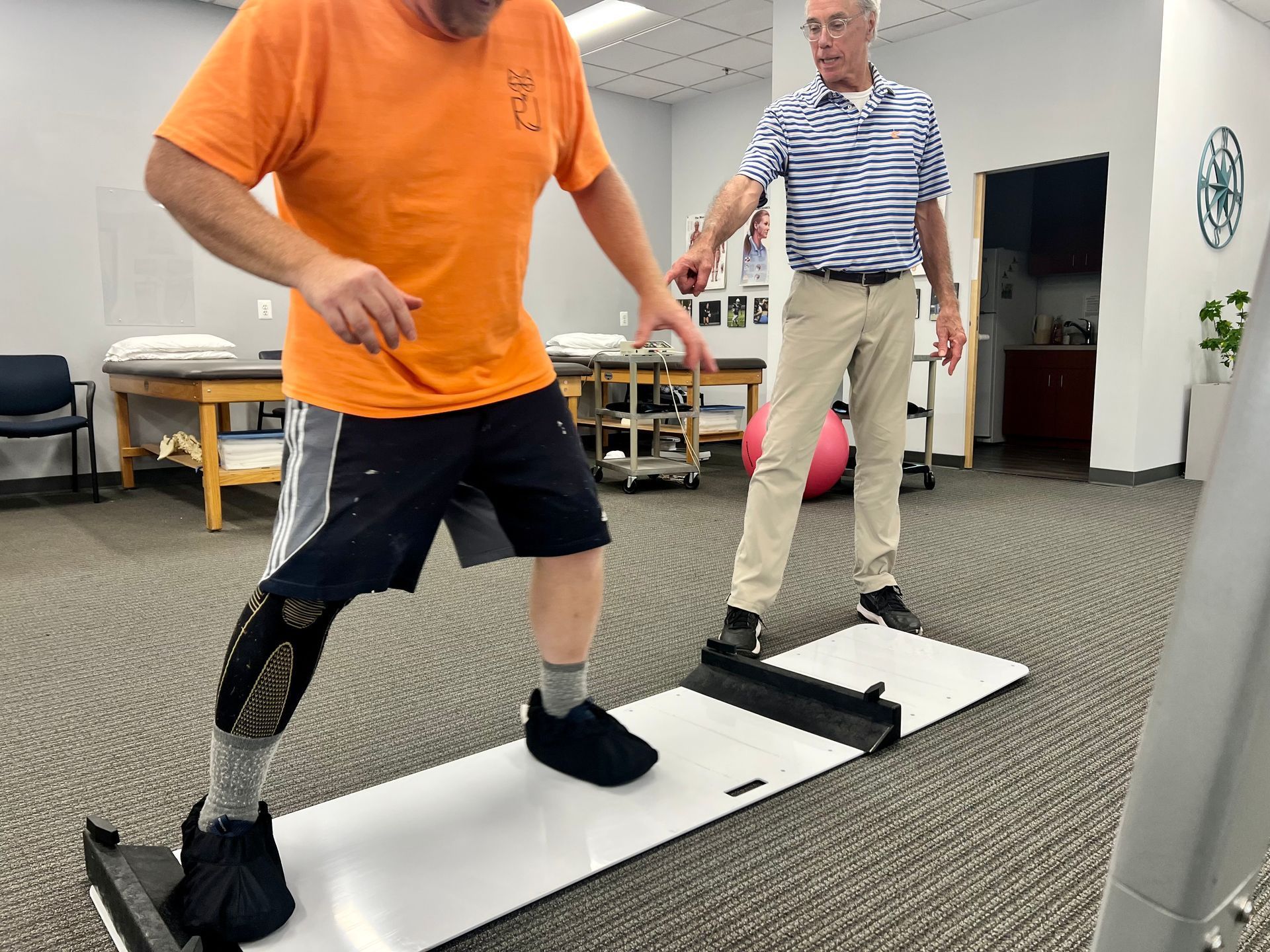 Man with prosthetic leg practicing balance on a platform, assisted by a therapist in a rehabilitation clinic.