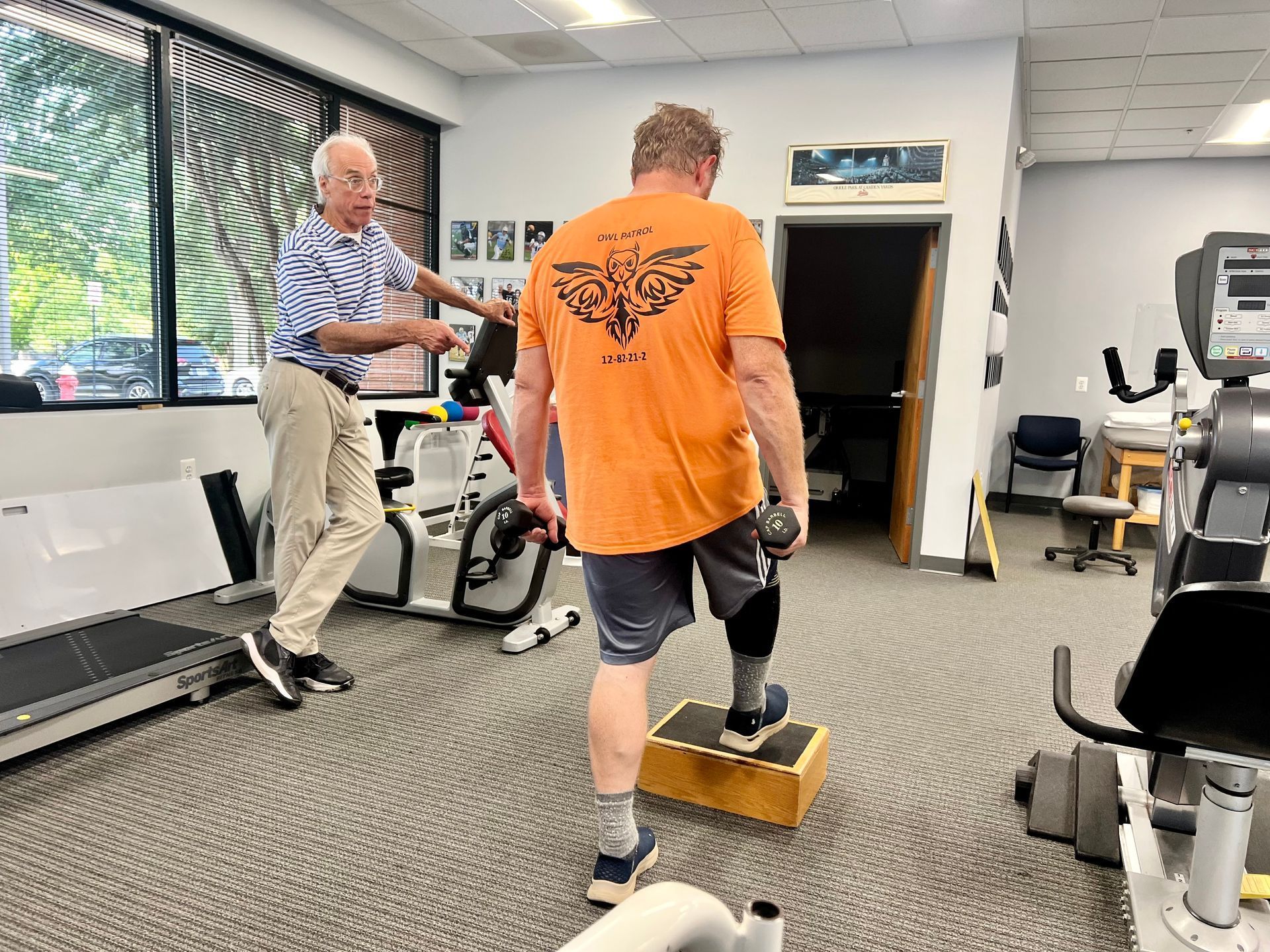 A man with a prosthetic leg steps onto a block with guidance from a therapist in a rehab center.
