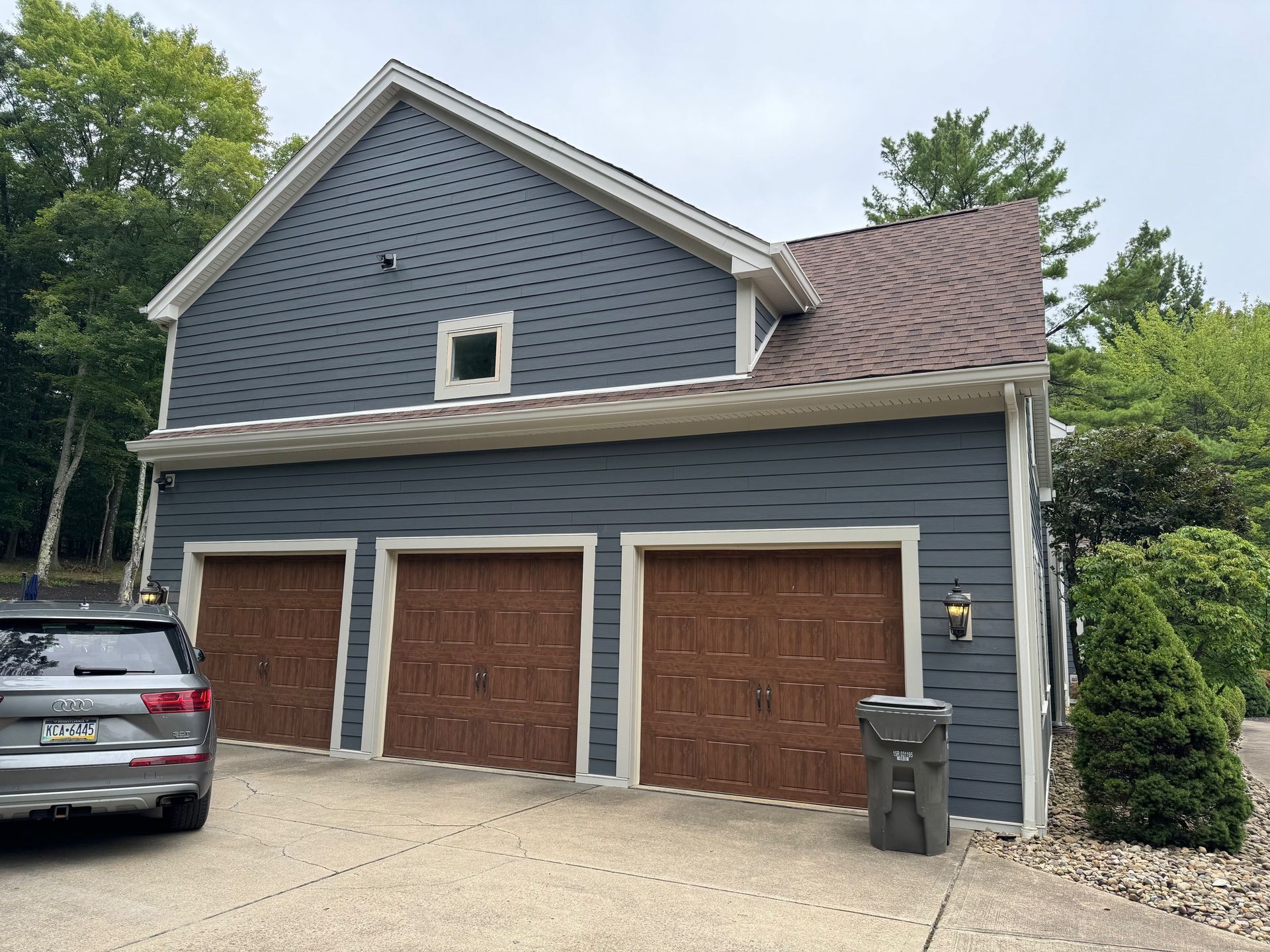 A car is parked in front of a garage with three garage doors.