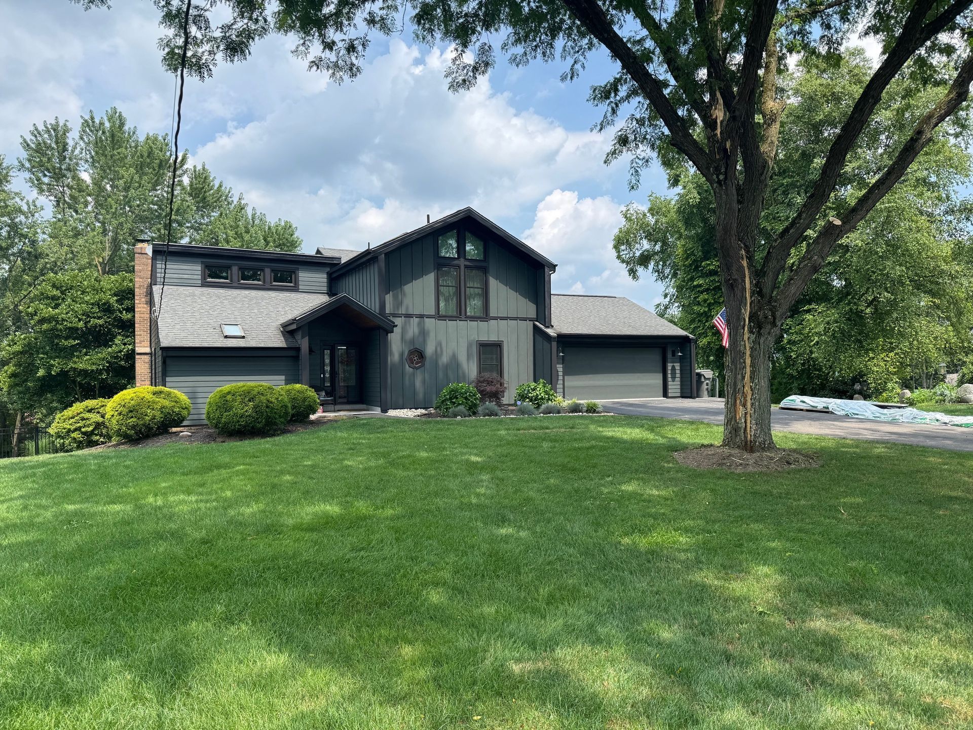 Green-painted house with a large lawn, trees, and a cloudy sky in the background.