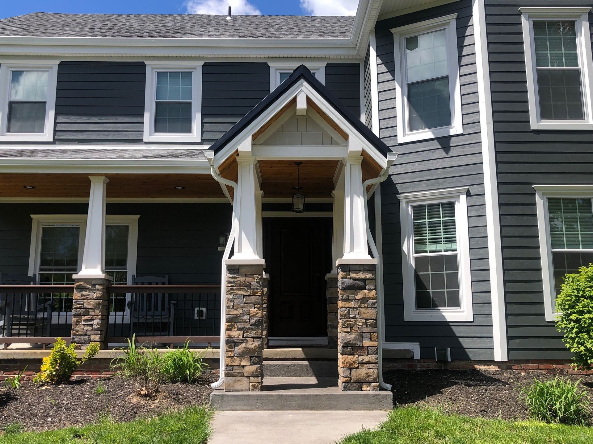 Dark blue house with white trim, stone columns, and covered entryway.
