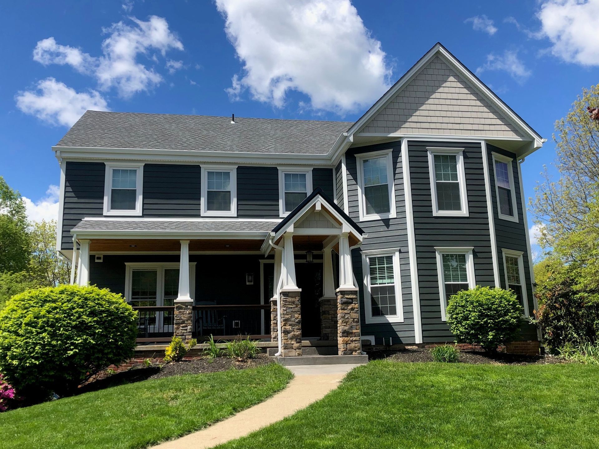 Two-story gray house with white trim, porch, and a gray roof under a blue sky with clouds.