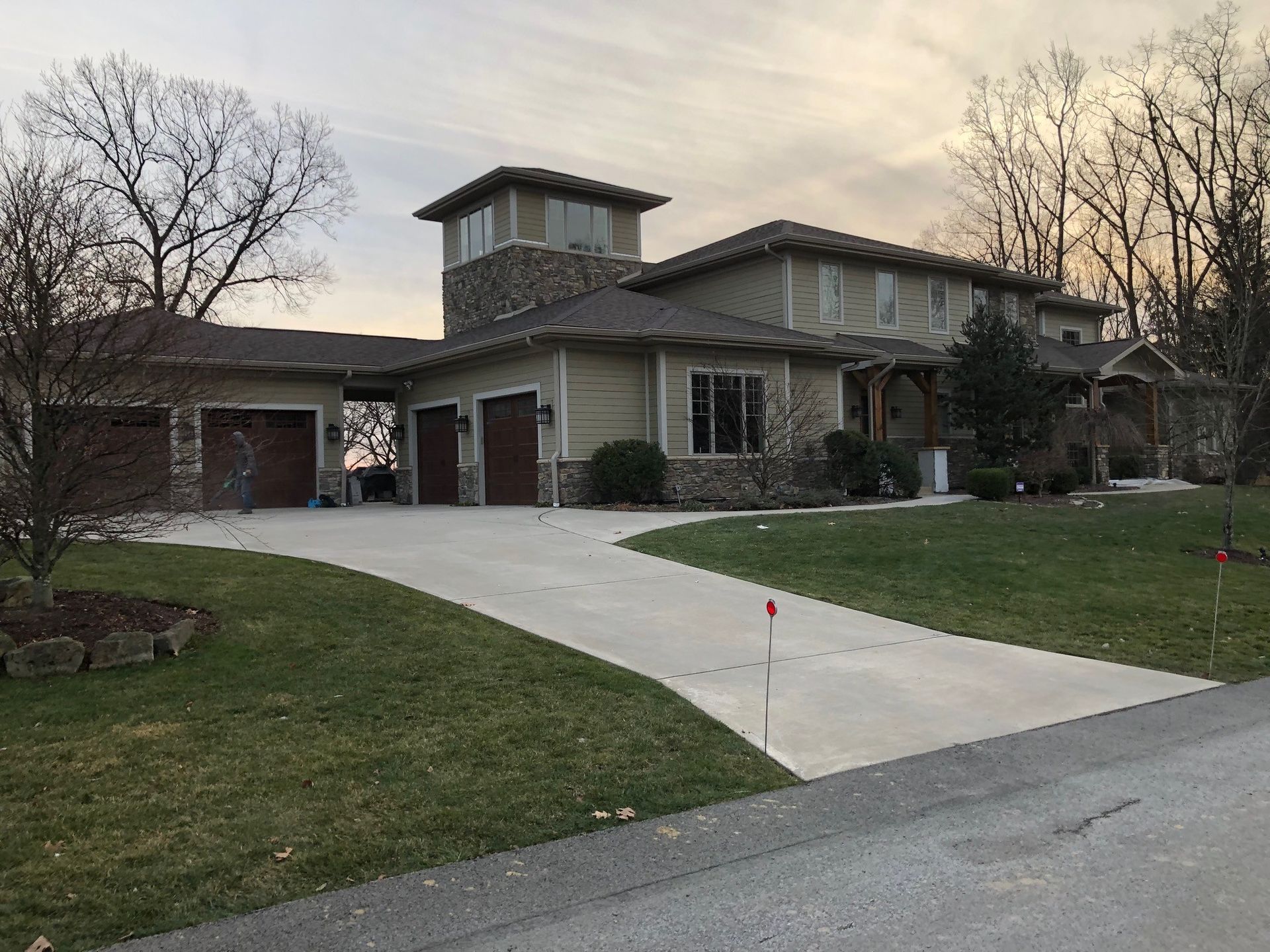 Beige house with a long driveway, attached garages, and a stone tower. Green lawn and trees.