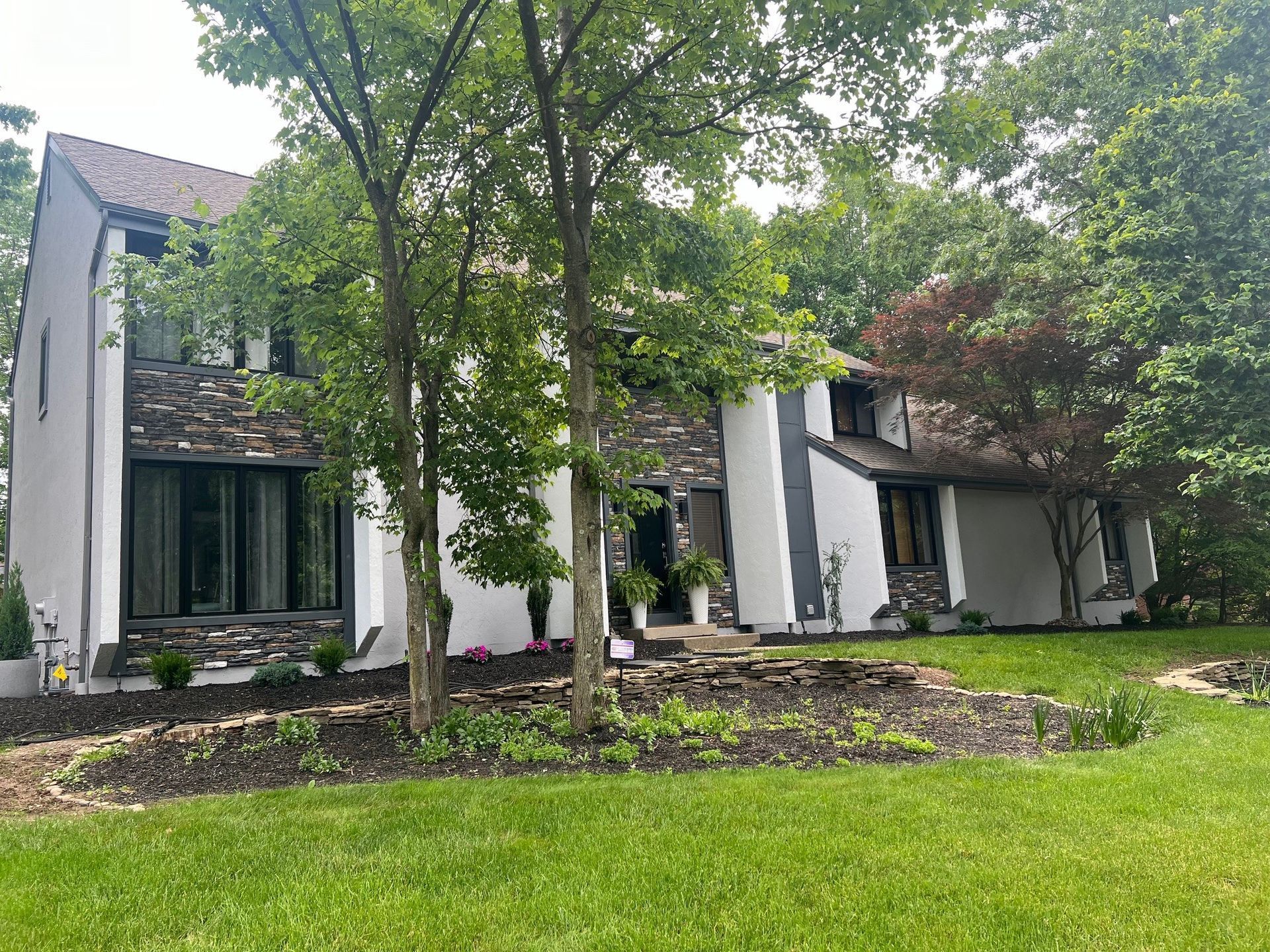A large white house with a stone facade is surrounded by trees and grass.
