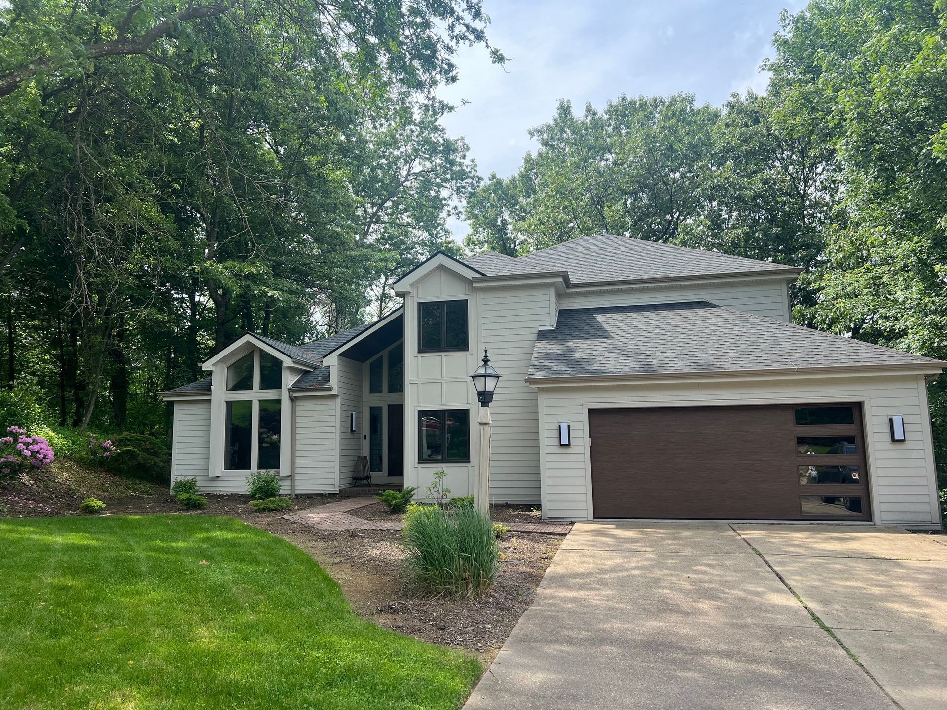 A large white house with a brown garage door is surrounded by trees.