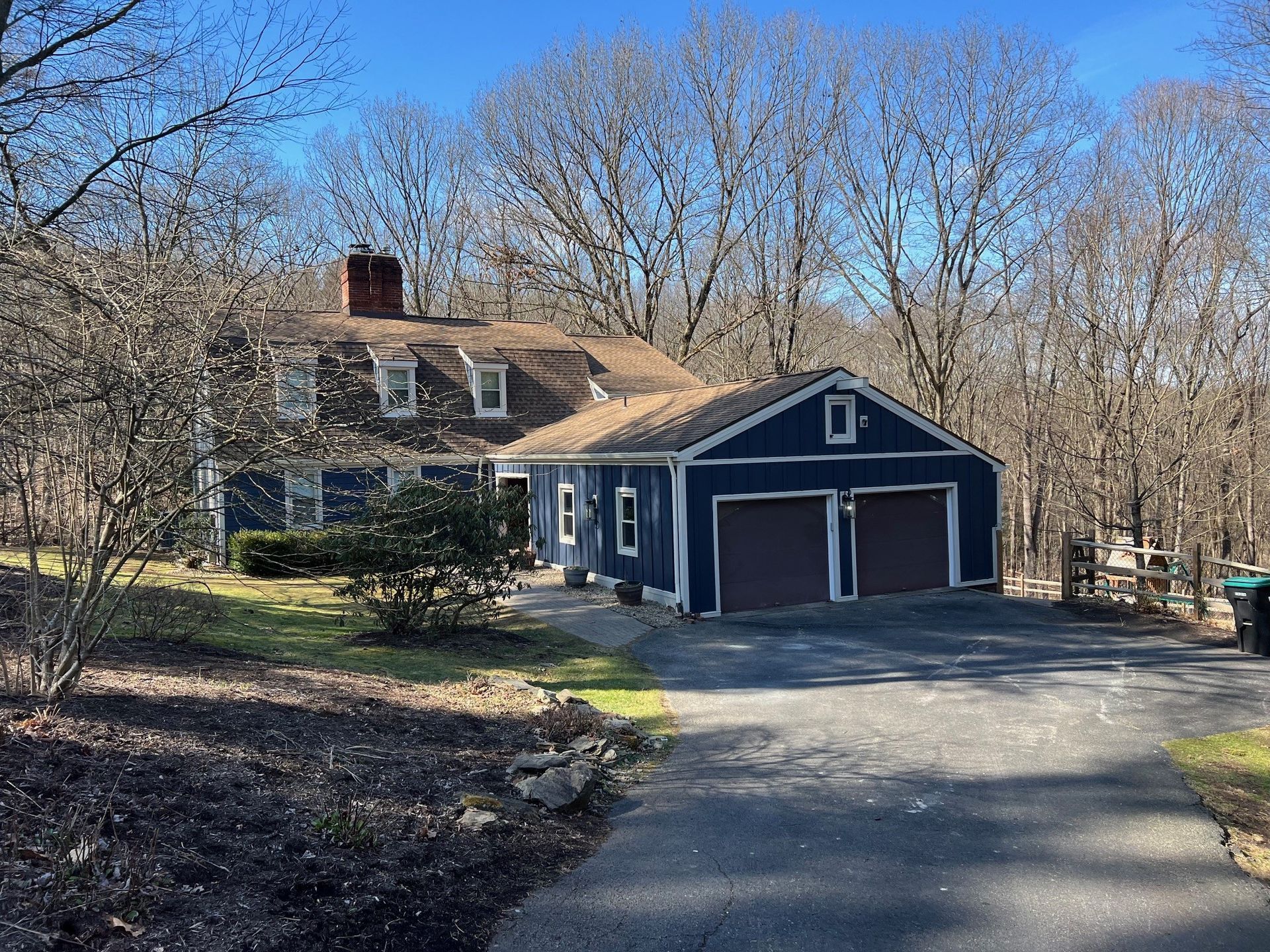 a blue house with a garage in the middle of a forest .