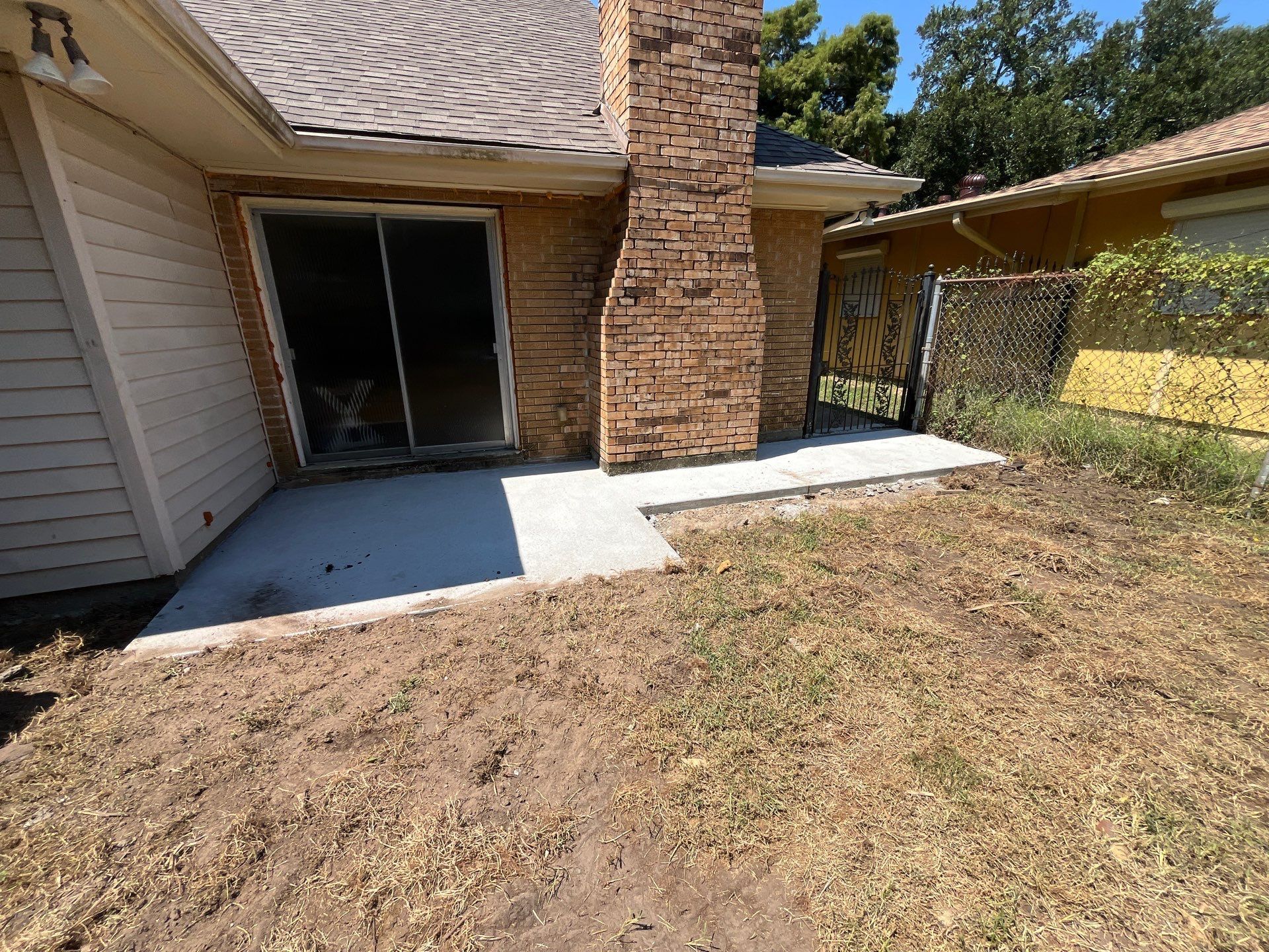 Backyard patio with a concrete slab, sliding glass door, and brick chimney.