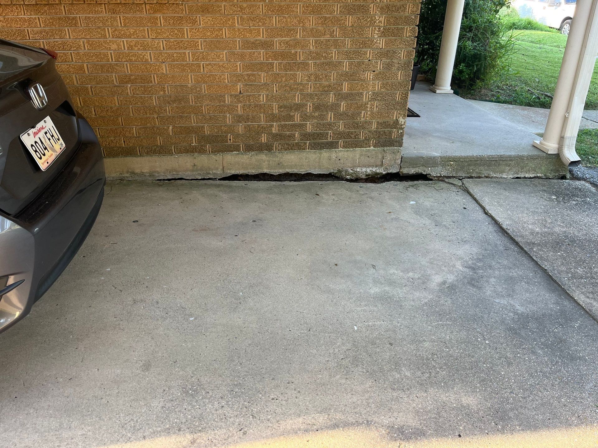 Concrete driveway next to a brick wall. A dark car is parked on the left side.