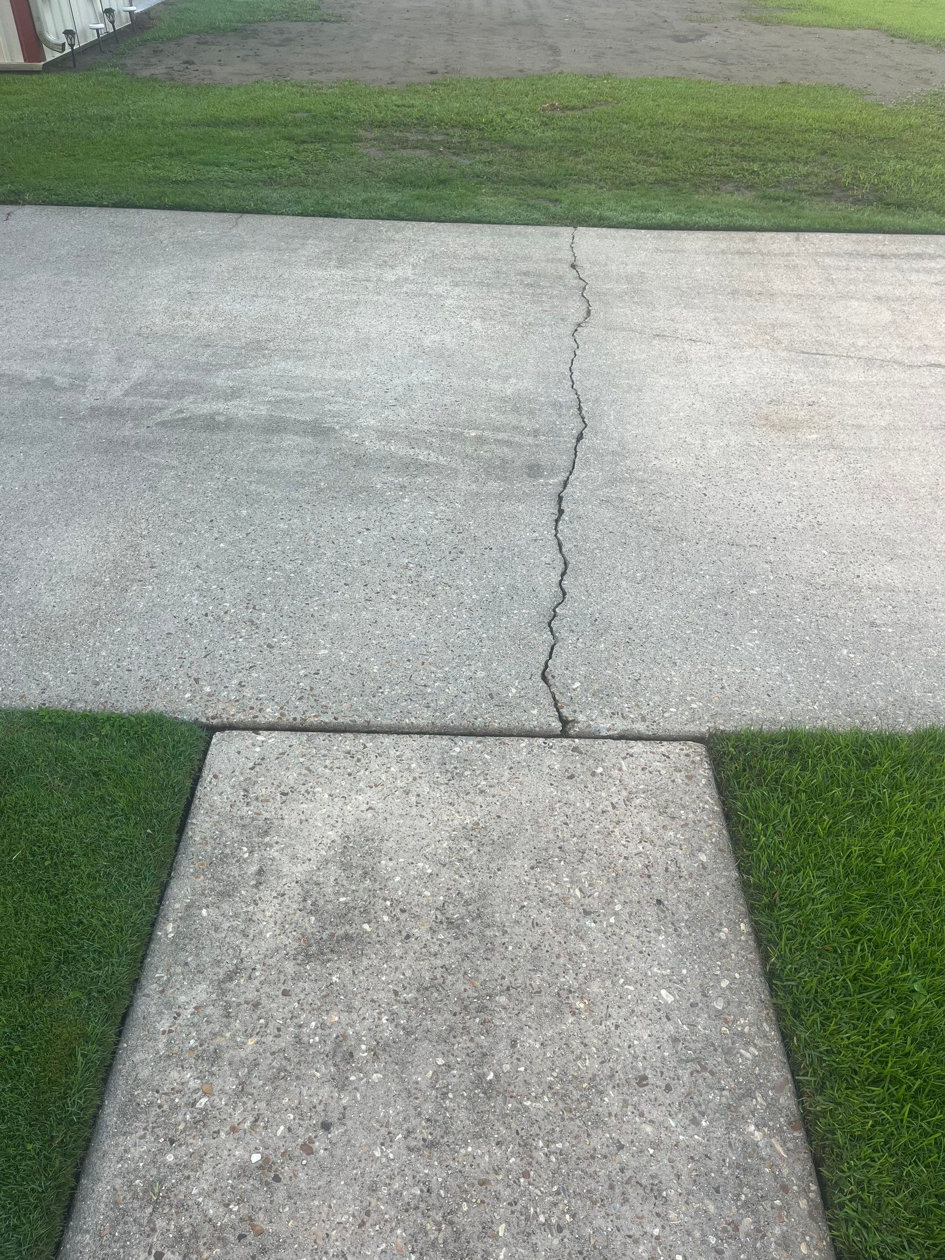 Concrete sidewalk with a crack, bordered by green grass.