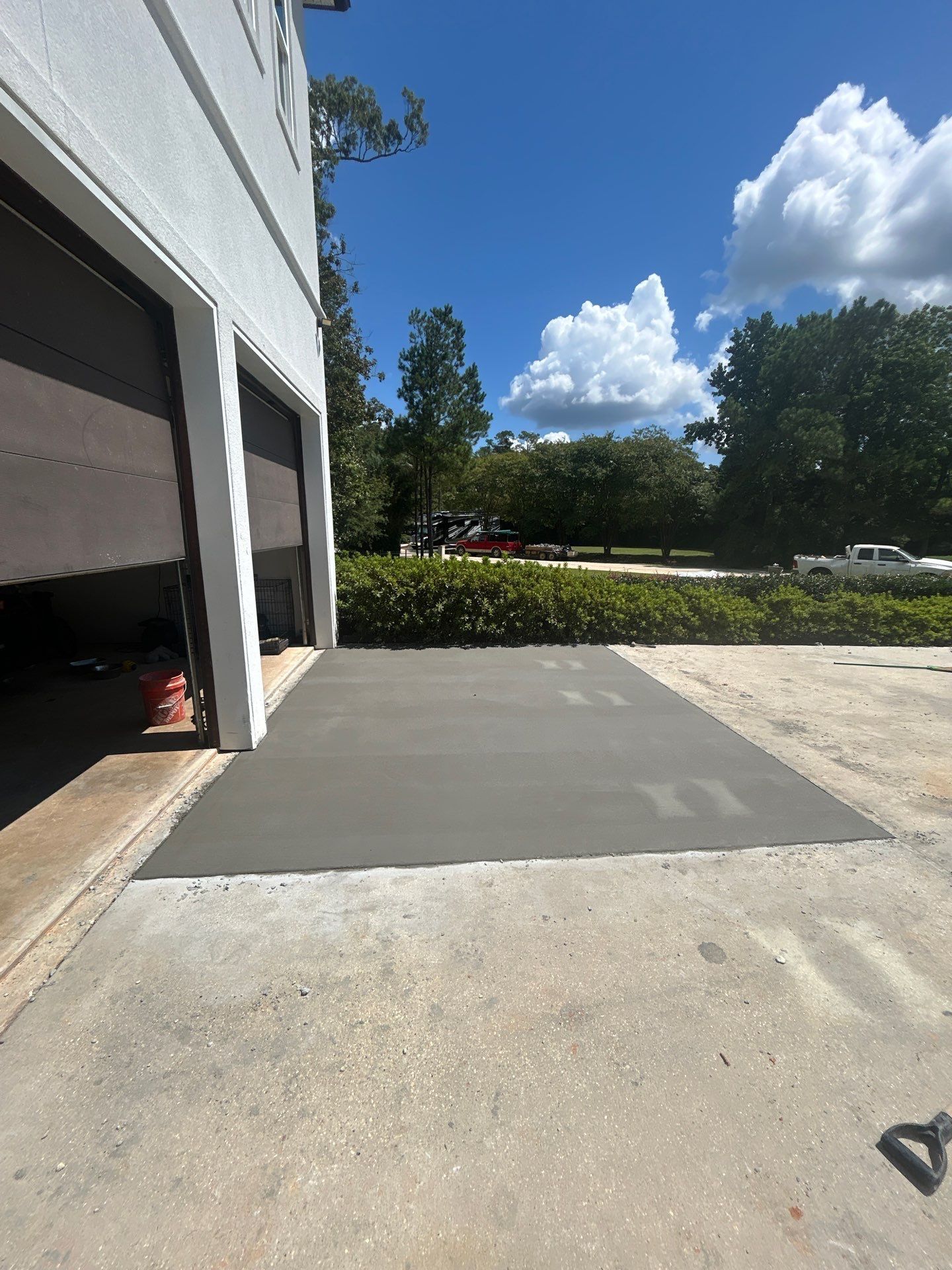 Freshly poured gray concrete patch in front of a garage, contrasting with the existing driveway under a sunny sky.
