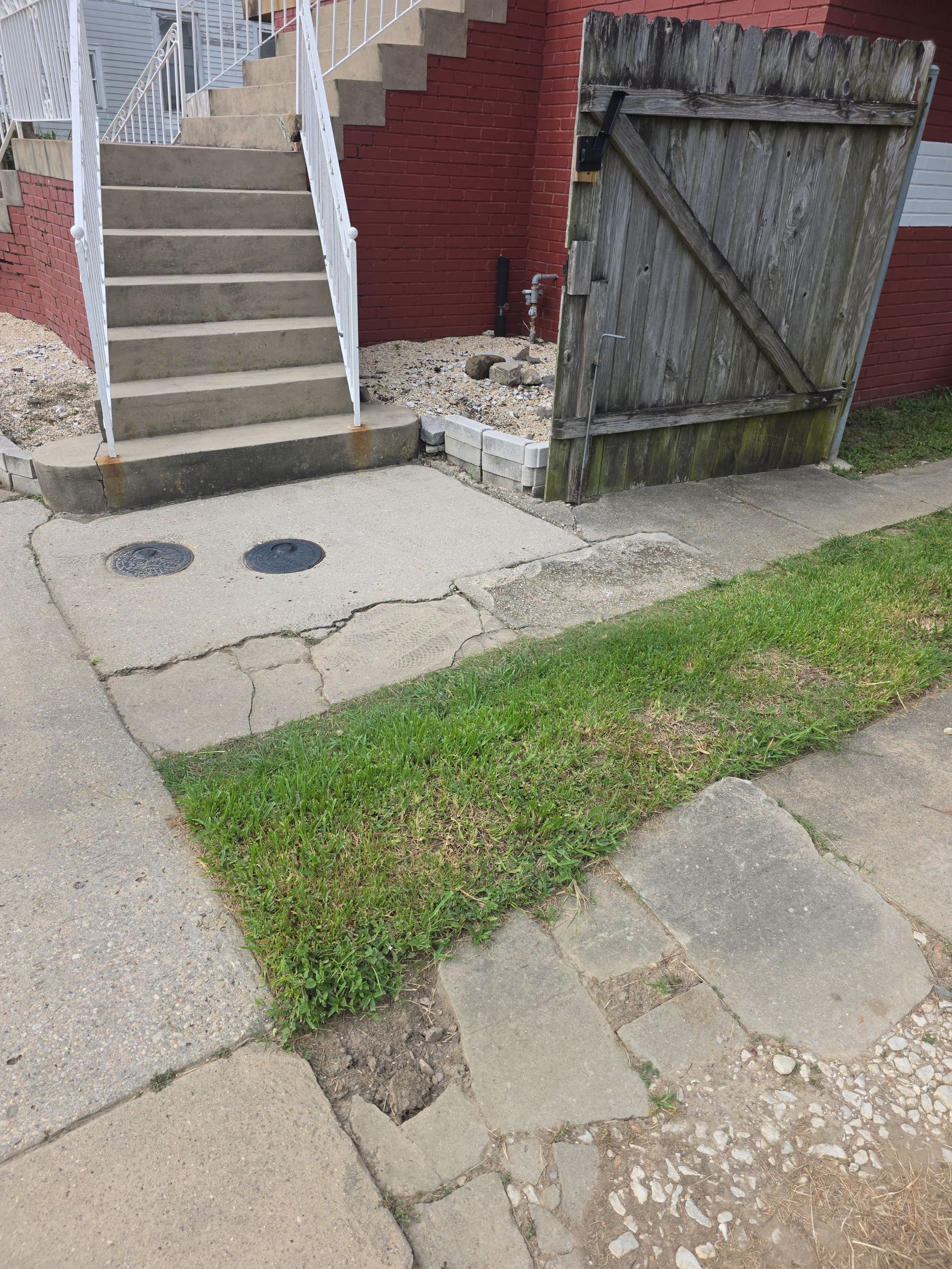 Concrete steps leading up, cracked sidewalk, short grass, and wooden fence.