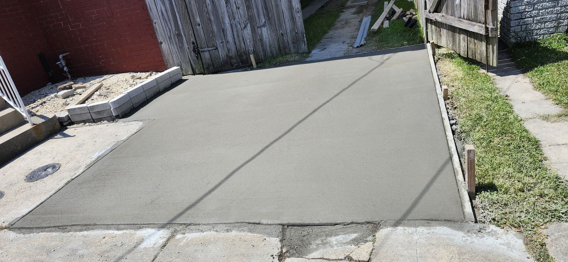 Freshly poured concrete driveway bordered by grass, fence, and steps.