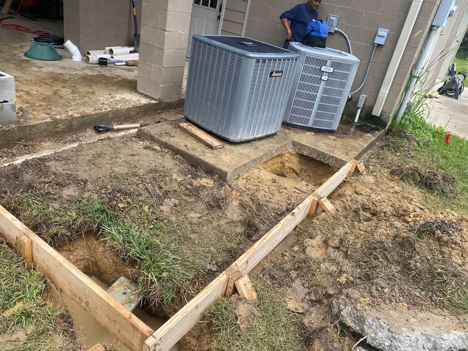 Construction site with air conditioning units and wooden framing for concrete work. A person works nearby.