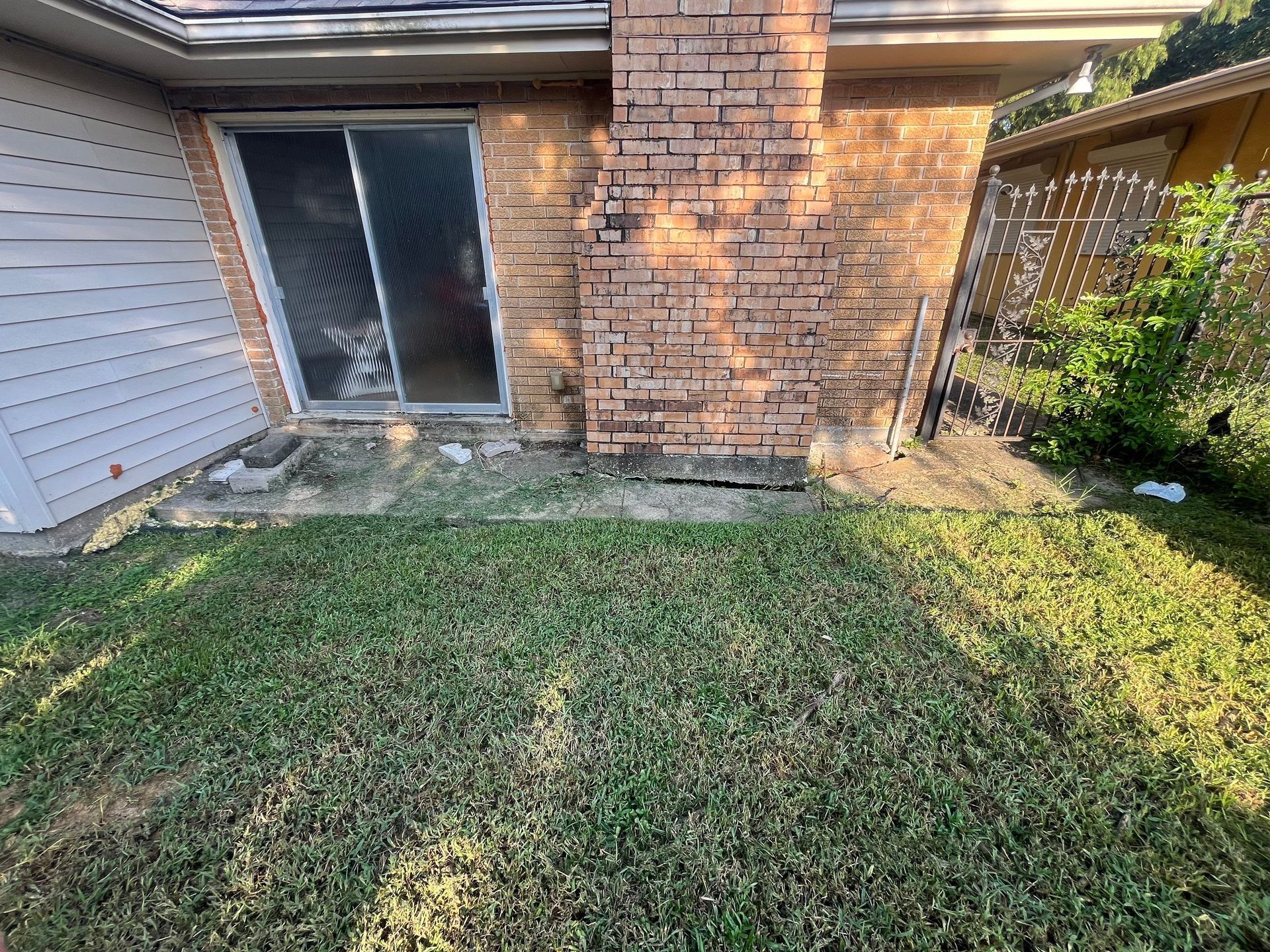 A brick chimney and sliding door next to a wooden fence and patchy grass.