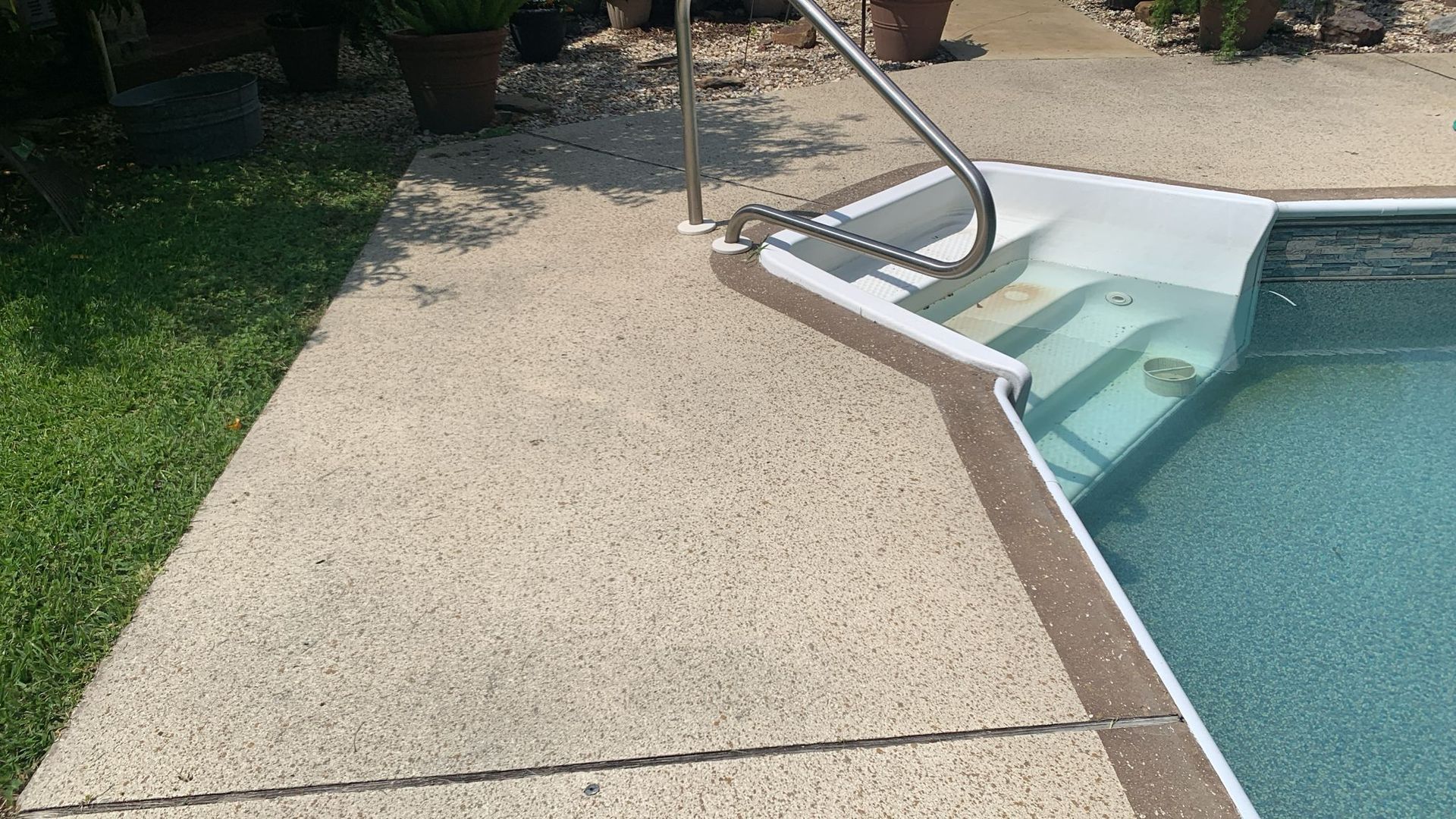 Poolside concrete path with a metal handrail leading into the water.
