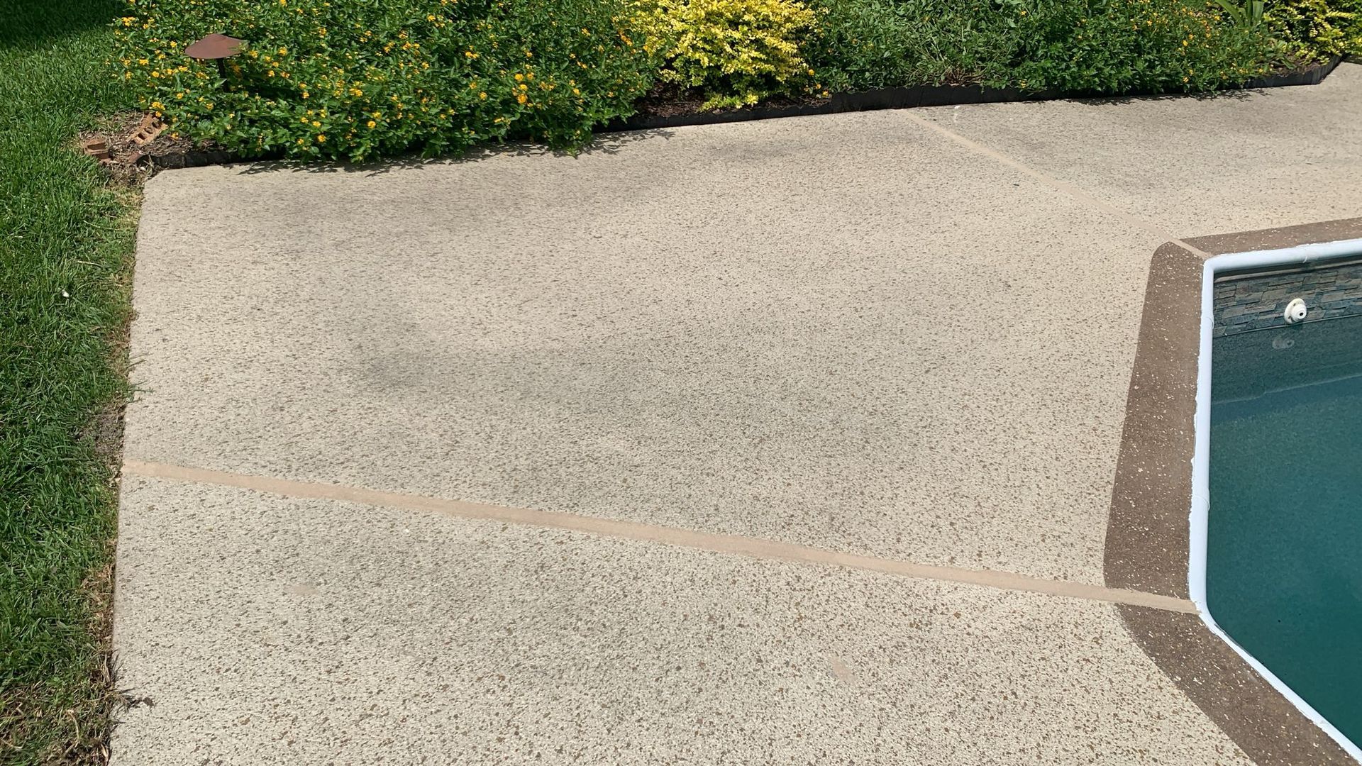 Concrete pool deck with cracks next to green grass and a turquoise pool.