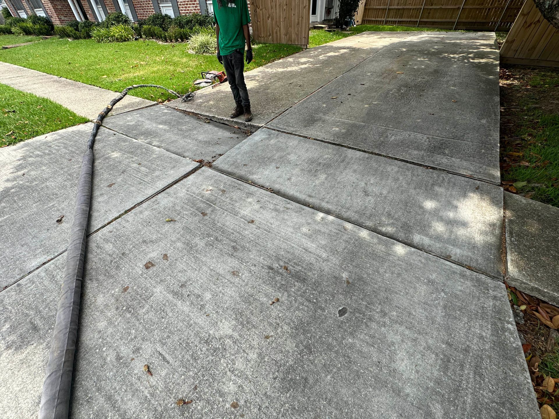 Cracked concrete driveway with large separation, green grass, and a person standing nearby.